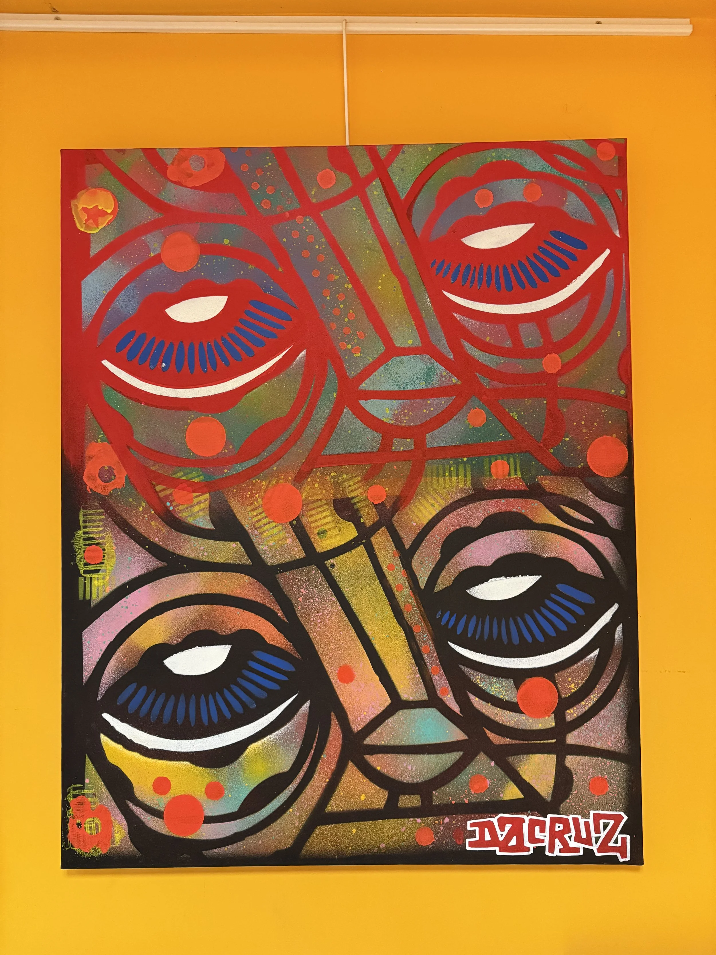 Peinture abstraite avec quatre visages stylisés en couleurs vives, notamment rouge, noir, blanc, rose, bleu, vert et jaune, sur un fond gris avec des taches de couleur. Signature en bas à droite.