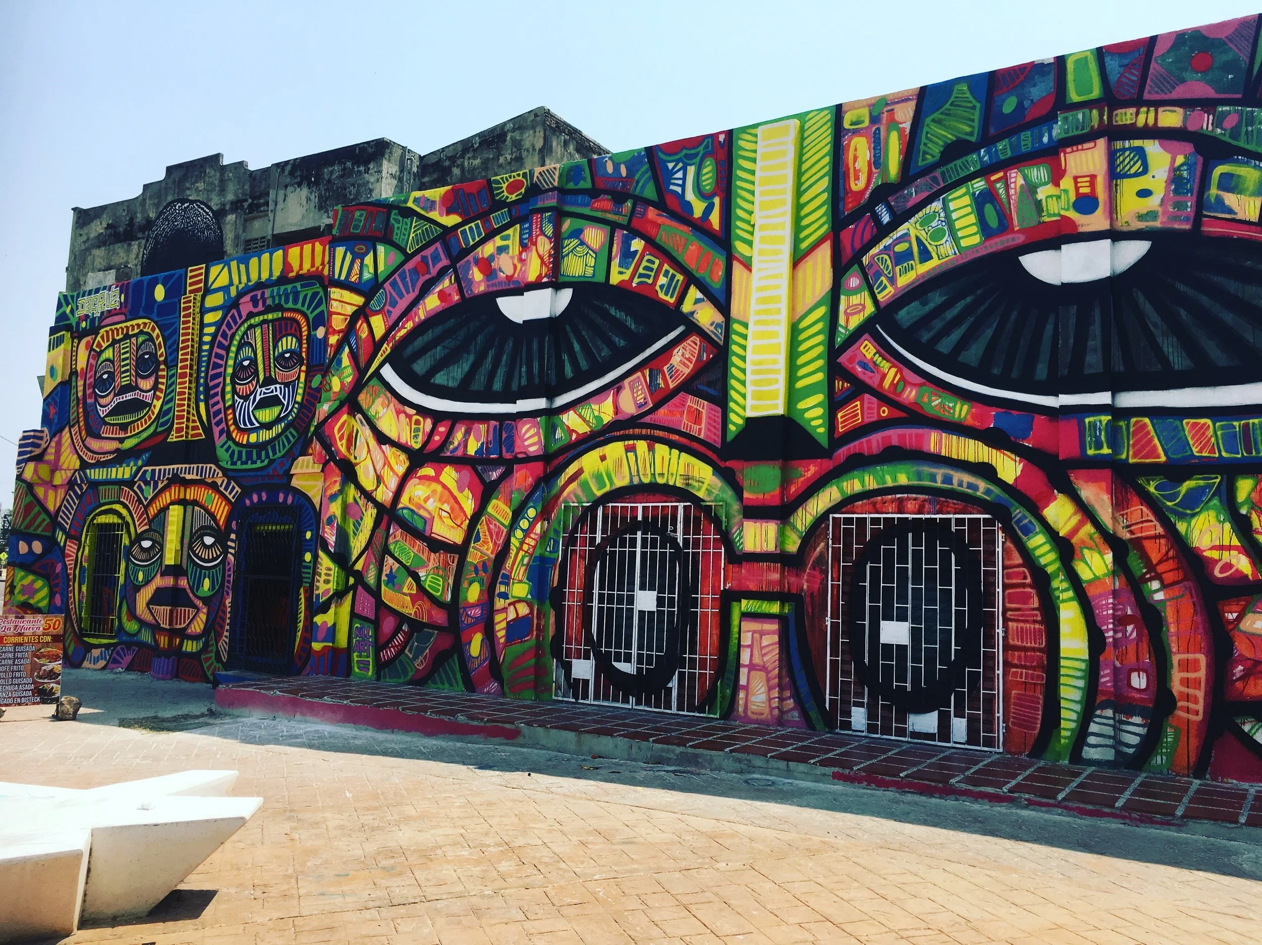 Mural coloré représentant un visage avec deux grands yeux, utilisant des formes géométriques et des couleurs vives.