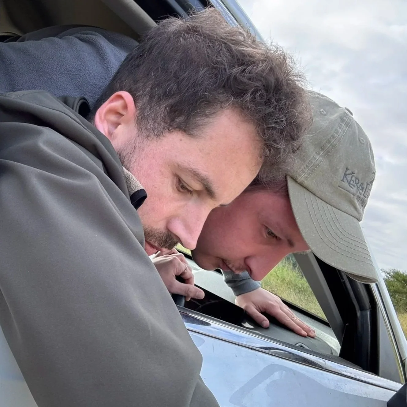 Deux hommes regardent par la fenêtre d'une voiture avec concentration.