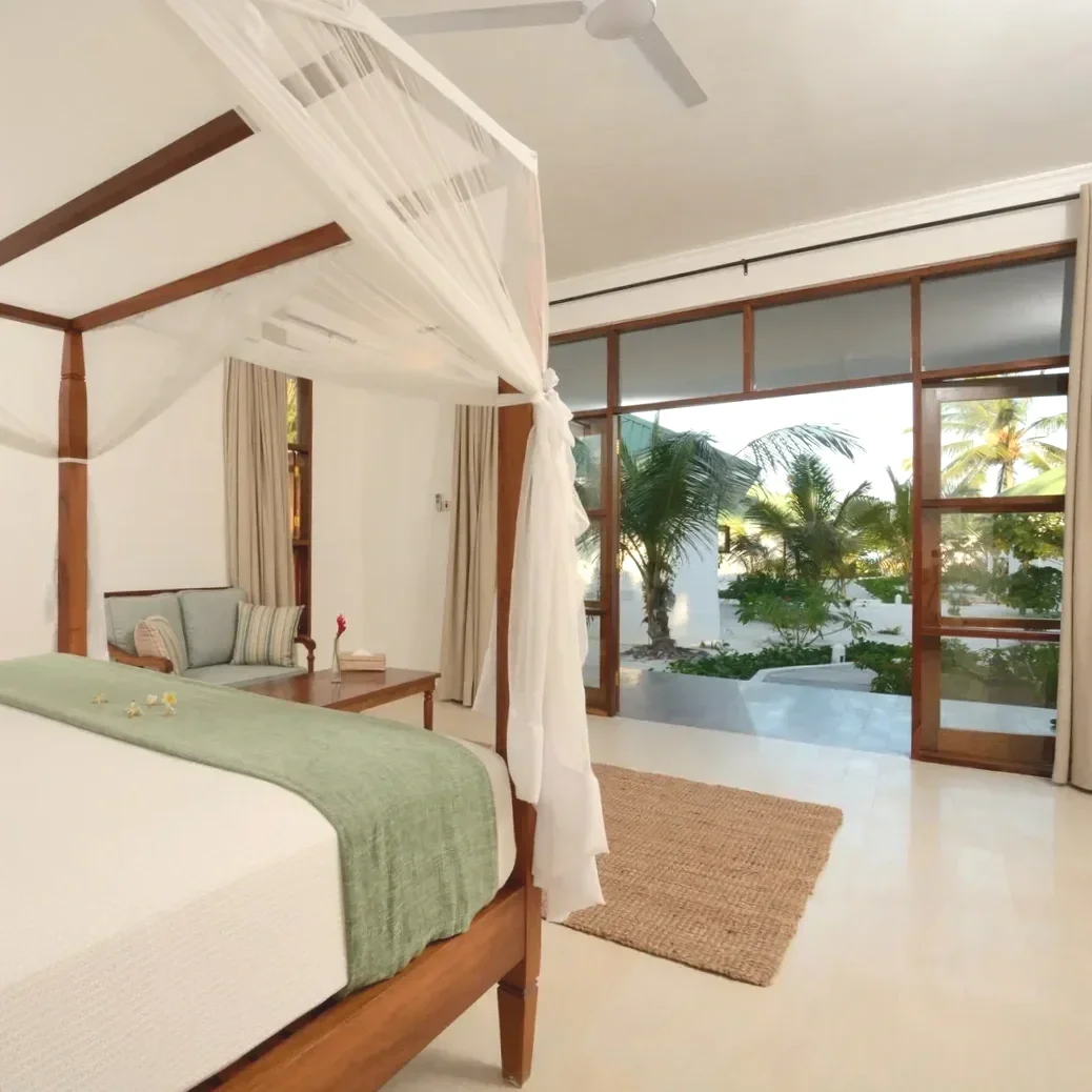 Chambre d'hôtel avec un lit à baldaquin, balcon avec vue sur des palmiers et un jardin tropical, décoration simple et élégante.