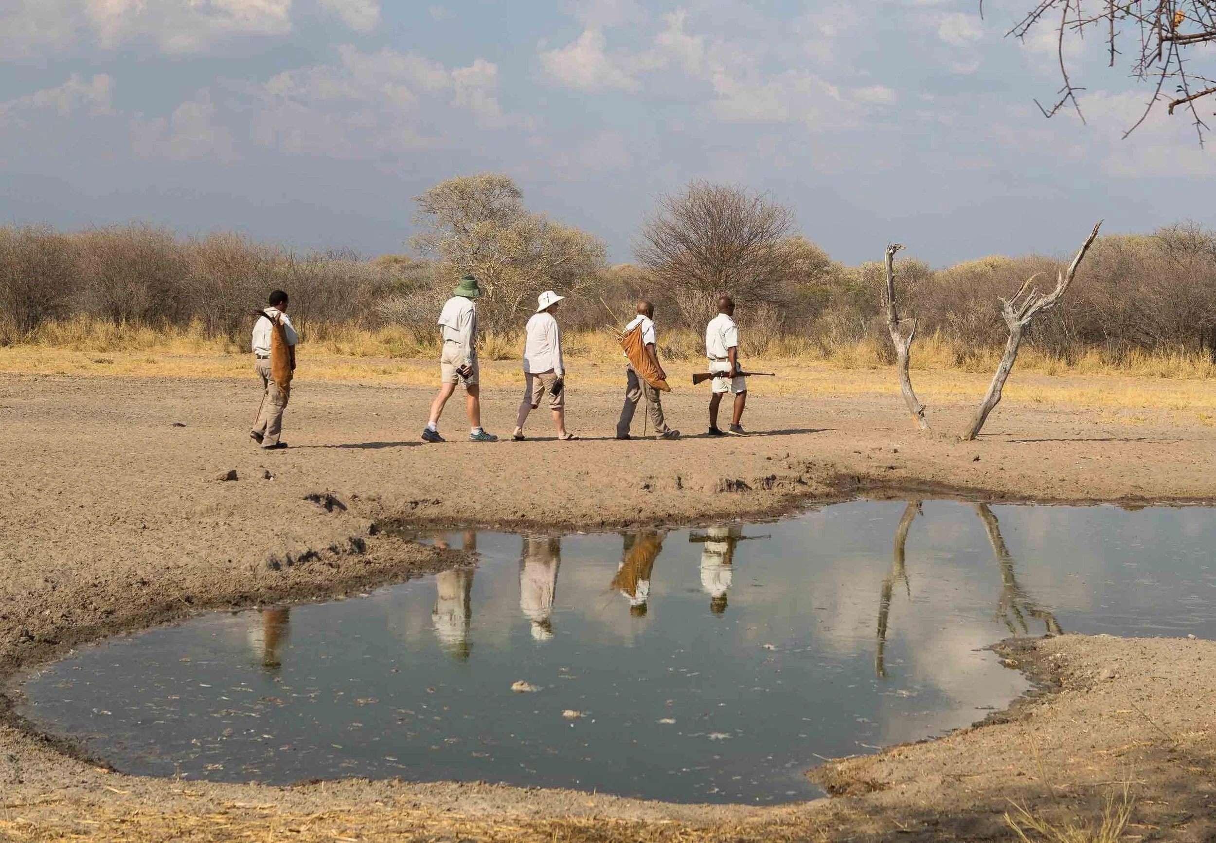 Groupe de cinq personnes portant des équipements de safari et marchant dans le désert du Kalahari au Botswana.