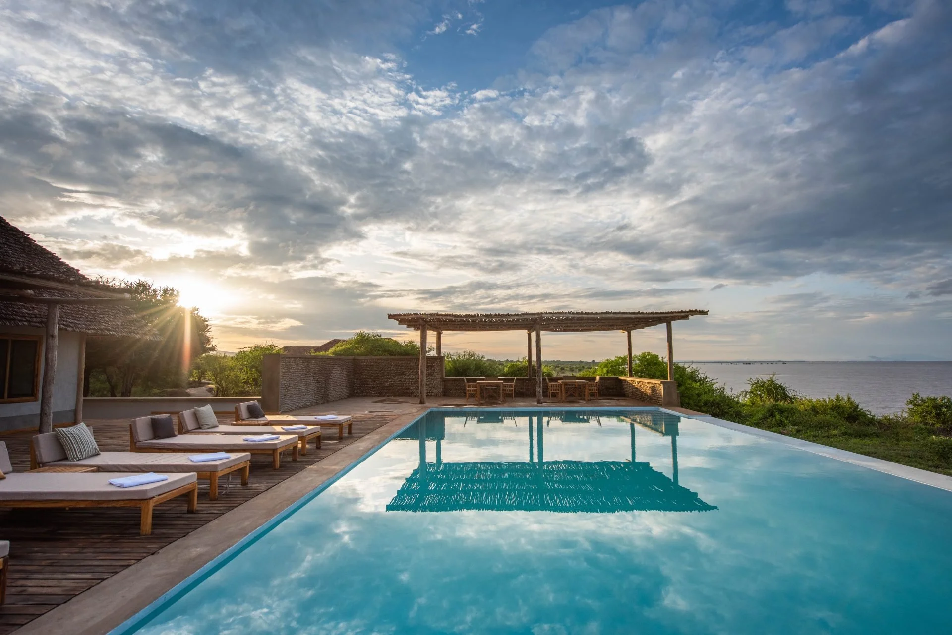 Piscine à l'extérieur avec des chaises longues en bois et un paysage de côte lors du coucher du soleil reflets dans l'eau