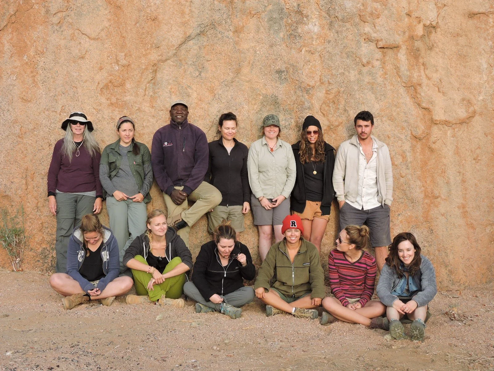 Volunteers posing for a group photo in front of a large, textured rock wall.
