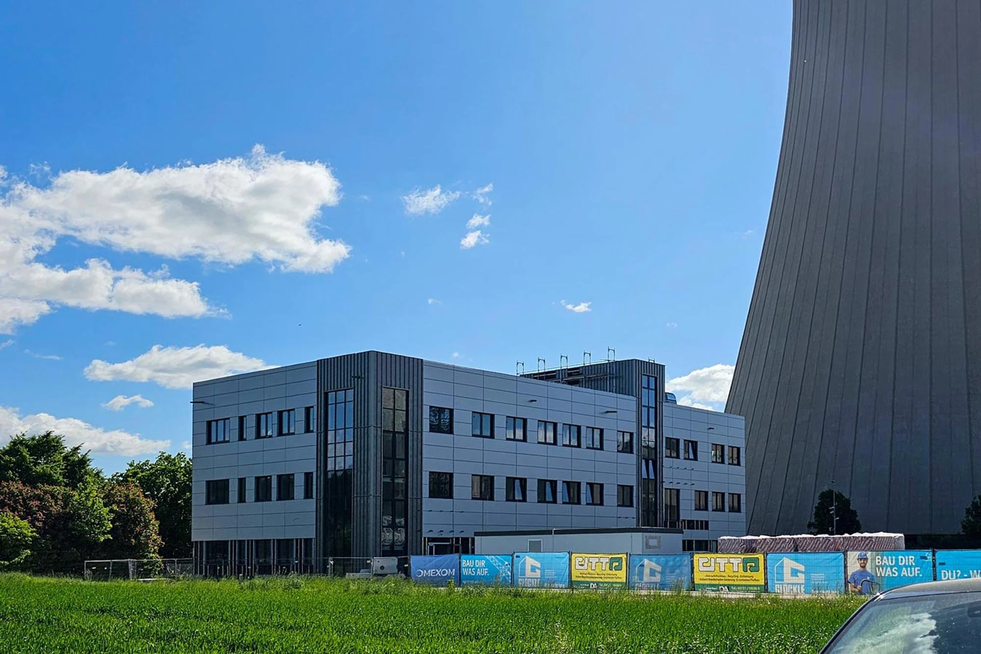 Neubau neben Kühltürmen mit weißer Paneelfassade und eingerüsteter Großbaustelle