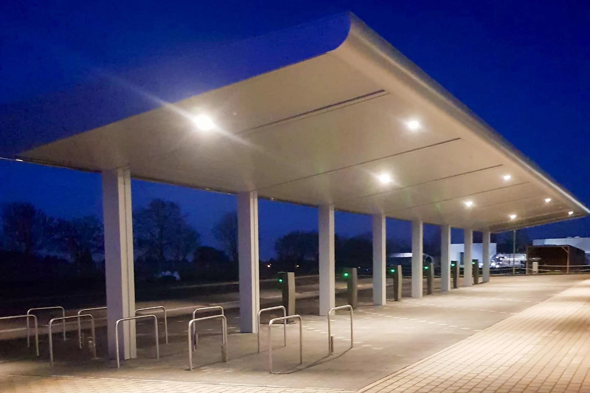 Überdachter Parkplatz mit Fahrradständern und E-Ladesäulen, beleuchtet bei Nacht