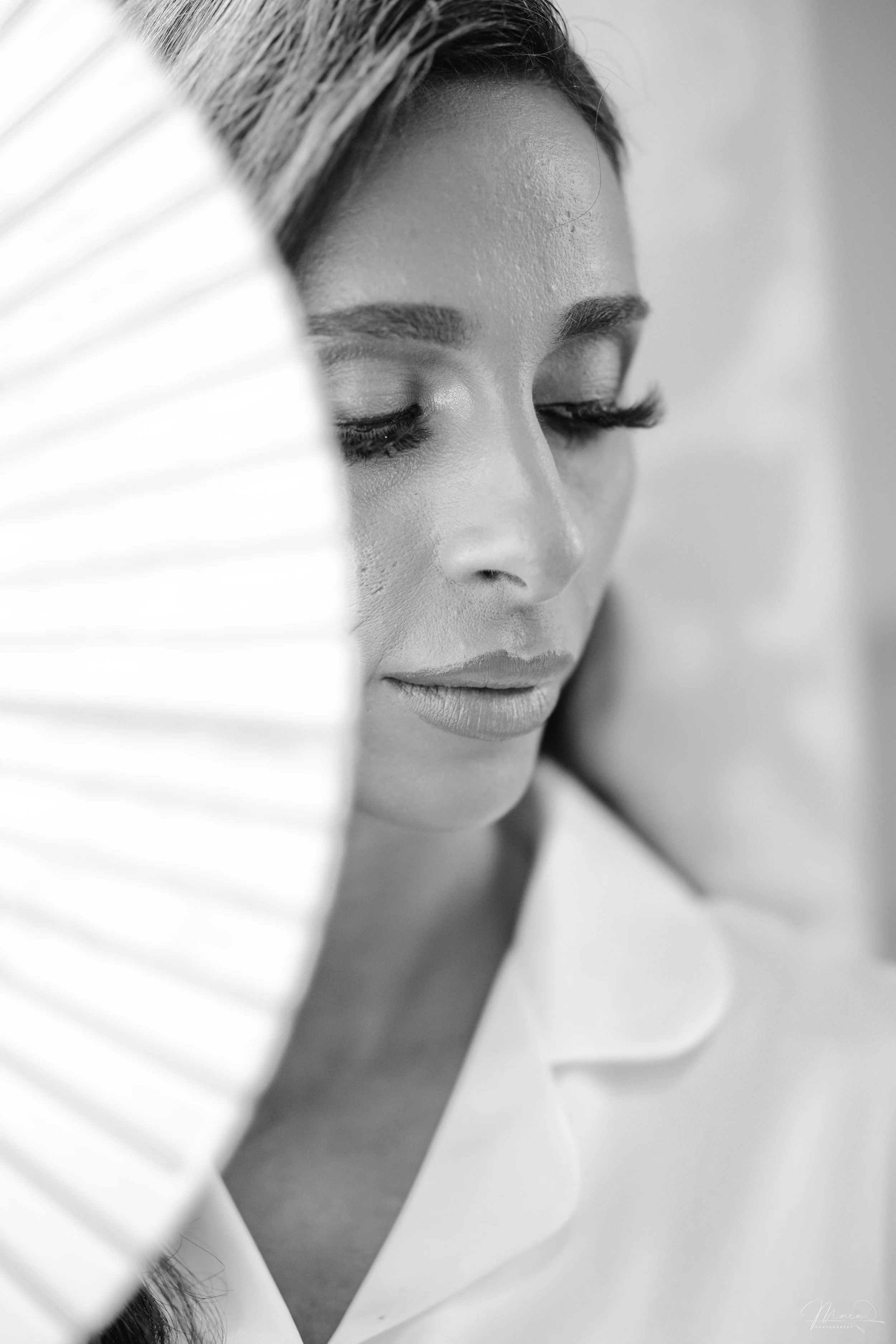 Close-up of a woman's face in black and white, with focus on her closed eyes and lips, partially obscured by a fan.