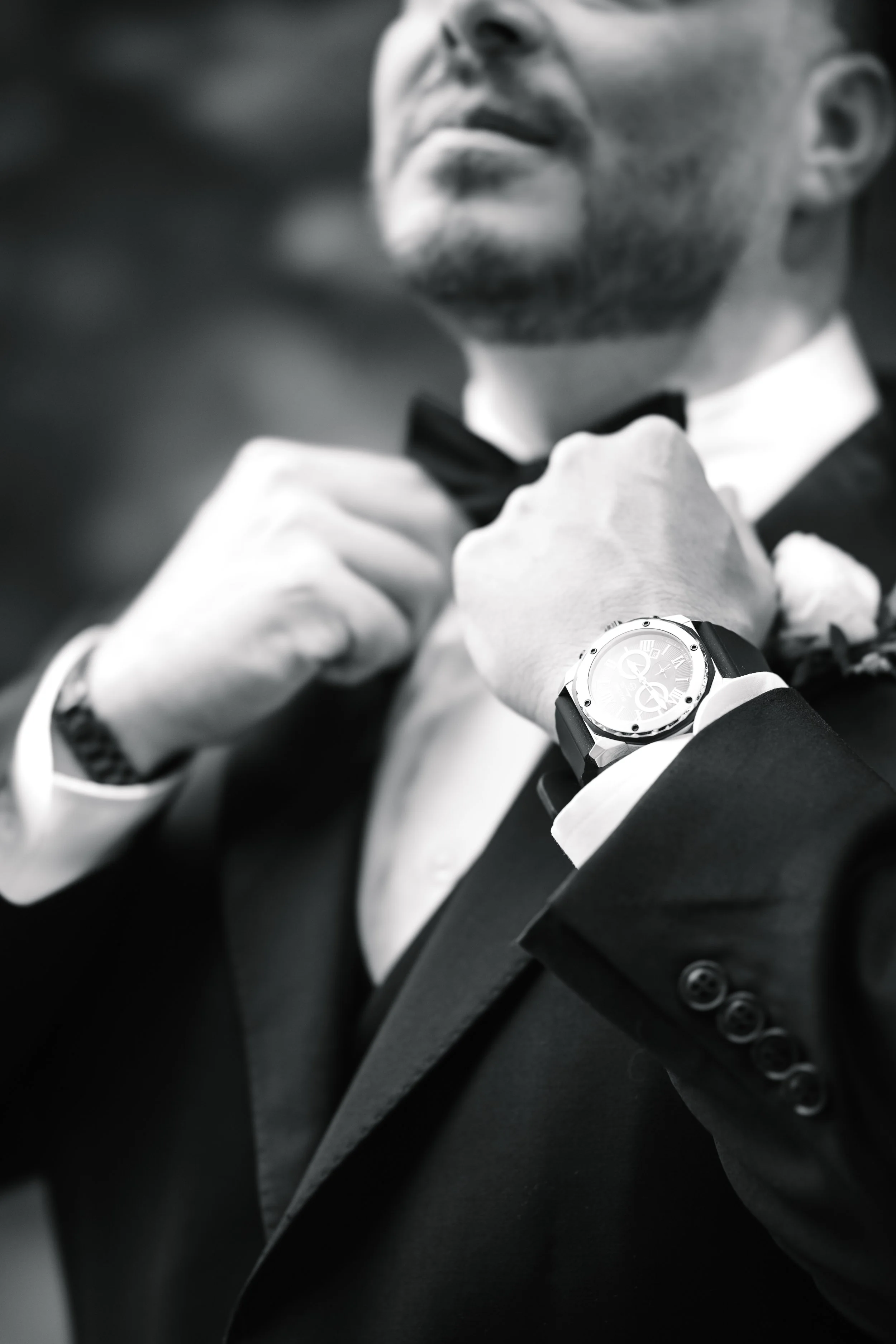 Man adjusting his bow tie while wearing a tuxedo and a wristwatch