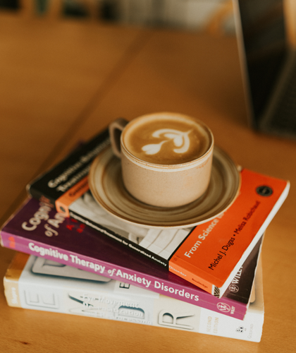 A cup of coffee with latte art on top, placed on a stack of three books on a wooden table.