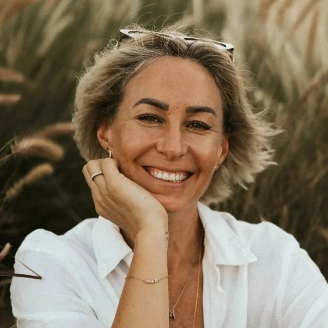 Kat Cuthbert EMDR & CBT Therapist BABCP Accredited, wearing a white shirt, sitting outdoors in a field of tall grasses.