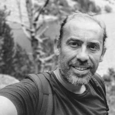 Hombre sonriendo con barba, mochila y camiseta en un entorno natural