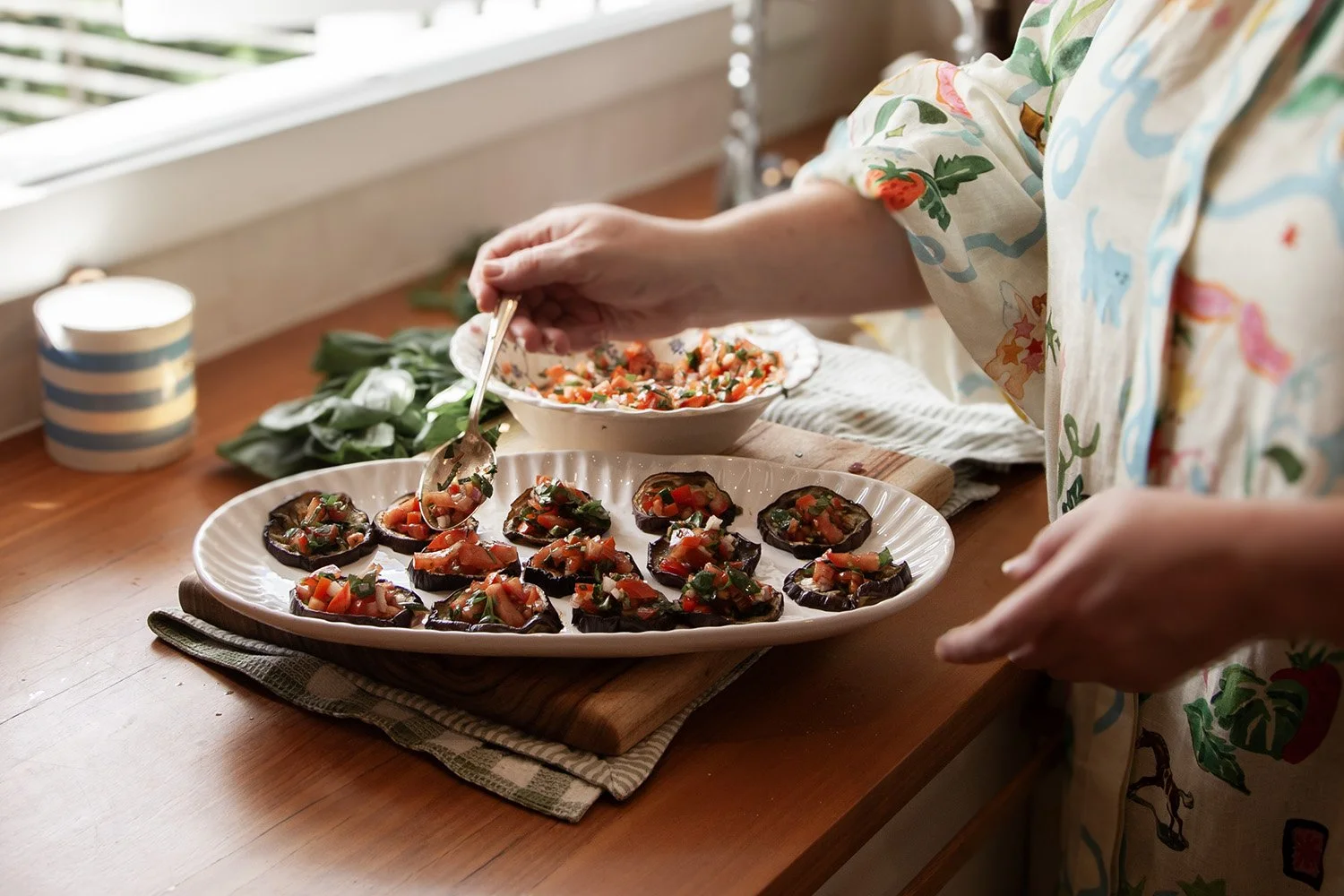 Person in kitchen making bruschetta on grilled eggplant for a dinner party