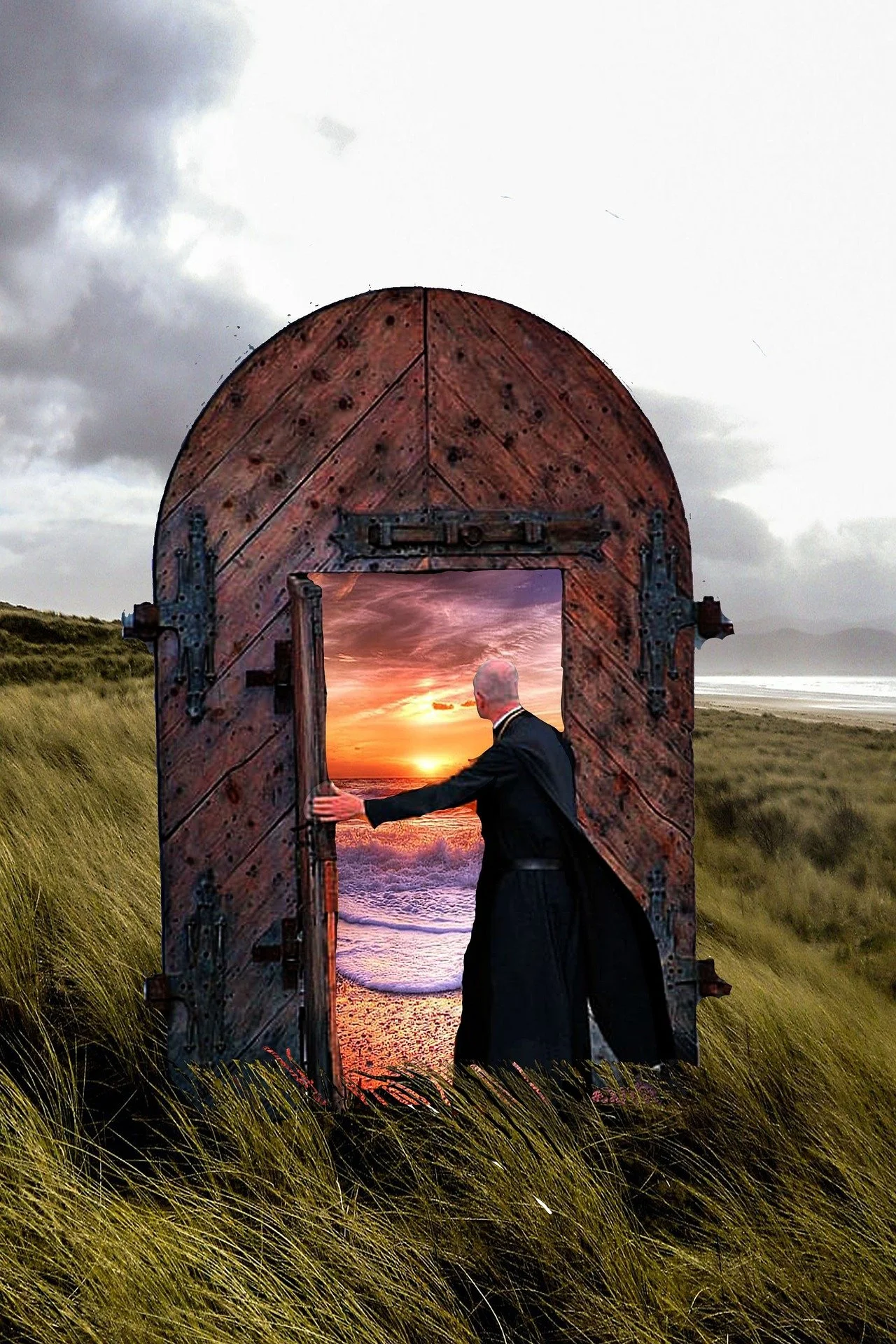 A man in a black coat opening a wooden door on a grassy field, revealing a sunset over the ocean.