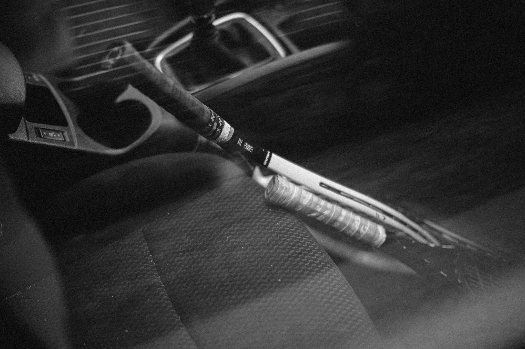 Black and white photograph of a car interior seen through a window, showing personal objects left inside.