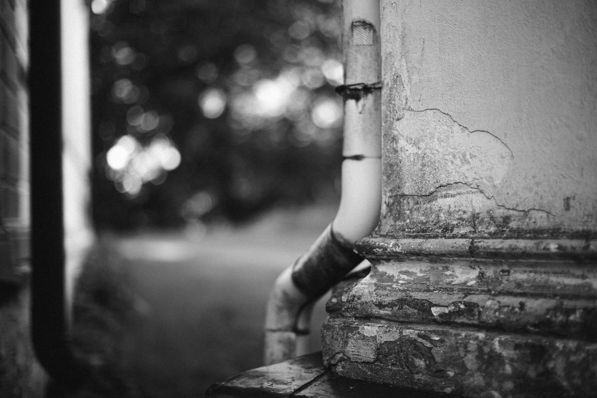 Cracked exterior wall with old drainpipe, black and white photograph of weathered architecture.
