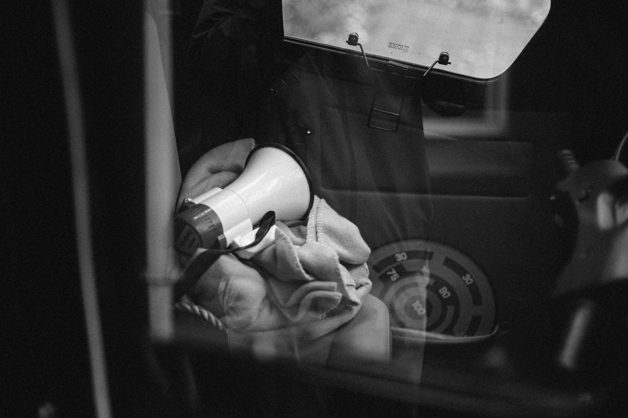 Black and white photograph of a car interior seen through a window, showing personal objects left inside.