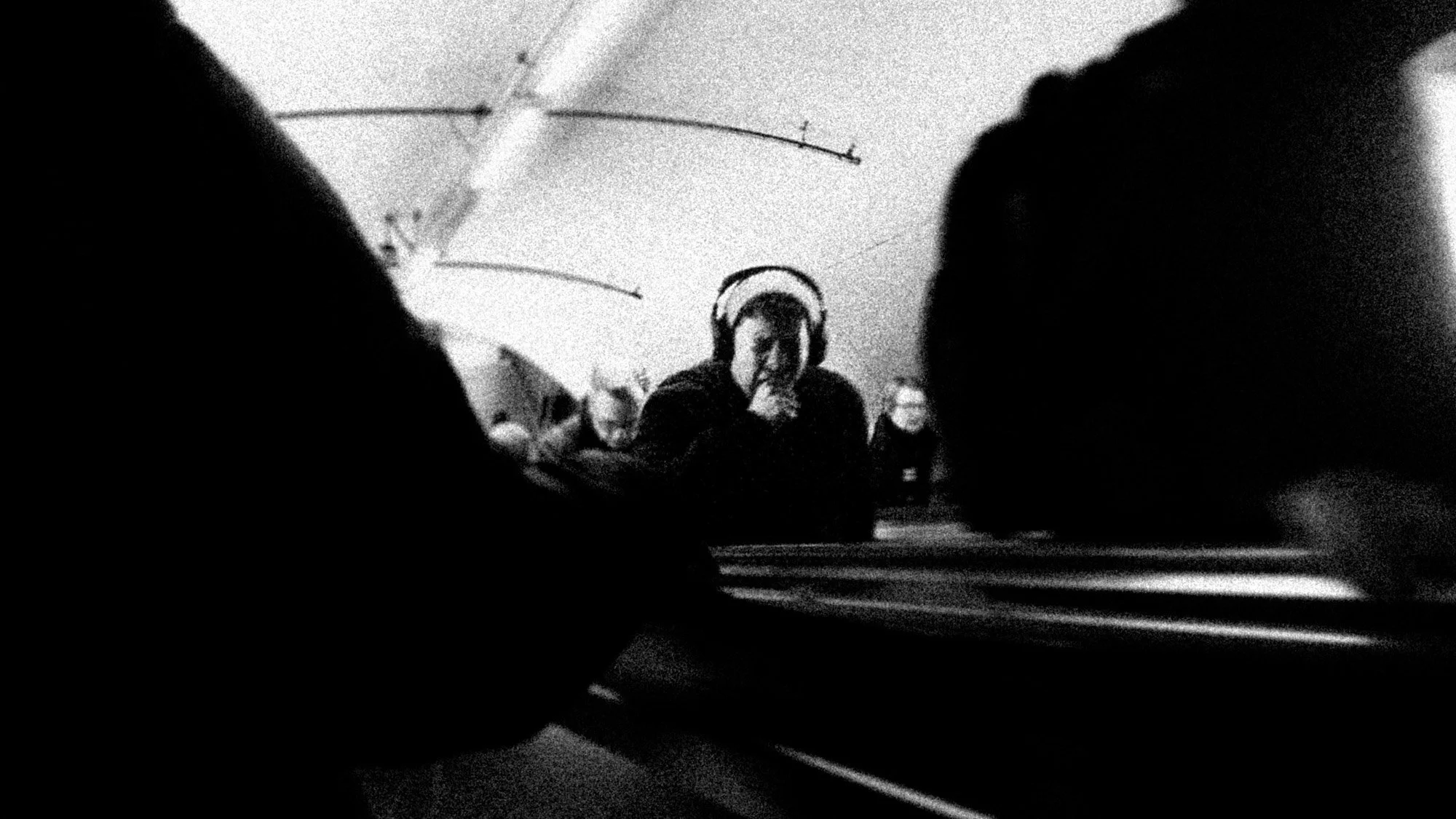 A tired person with headphones riding the escalator, yawning, surrounded by other people in the morning rush.