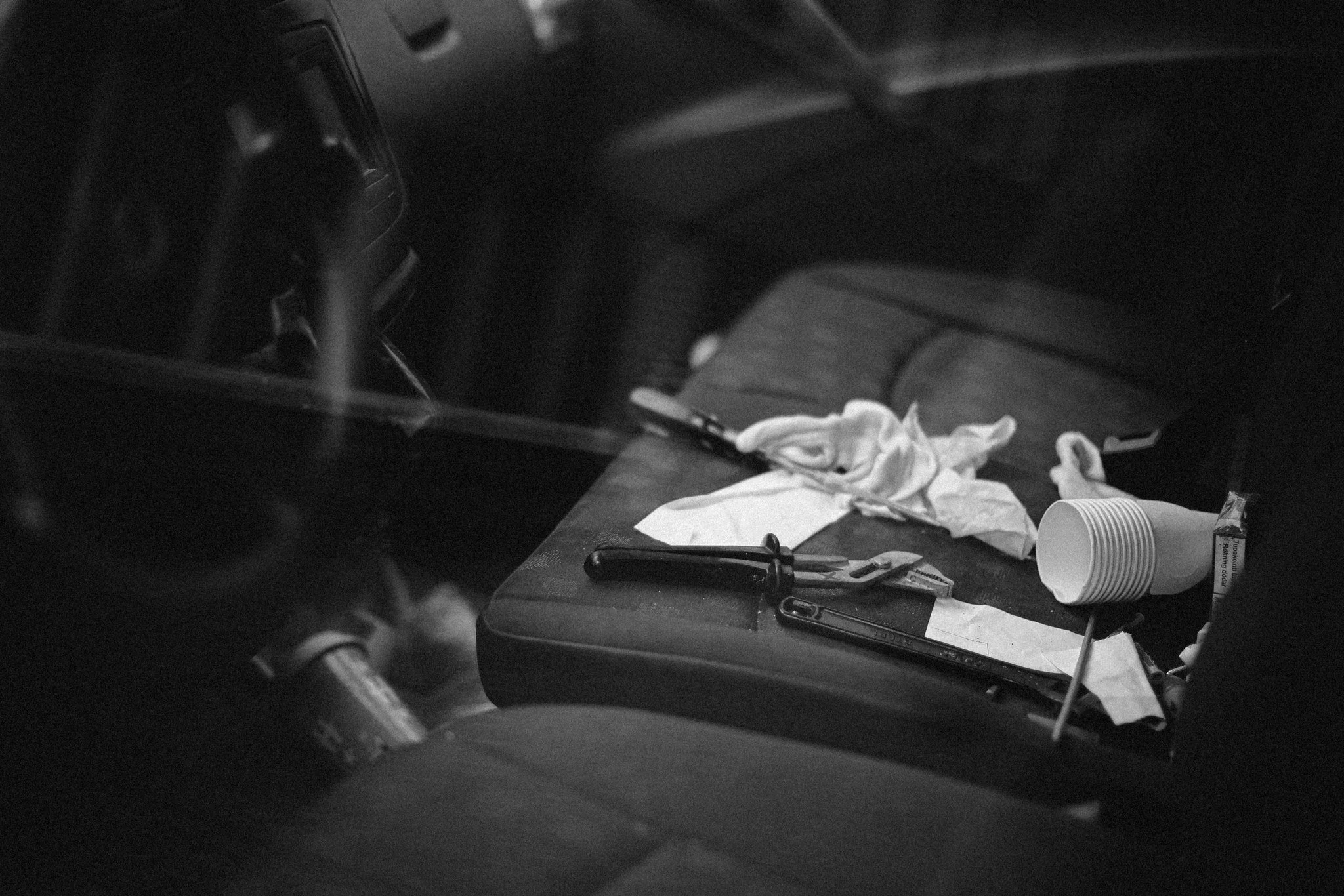 Black and white photograph of a car interior seen through a window, showing personal objects left inside.