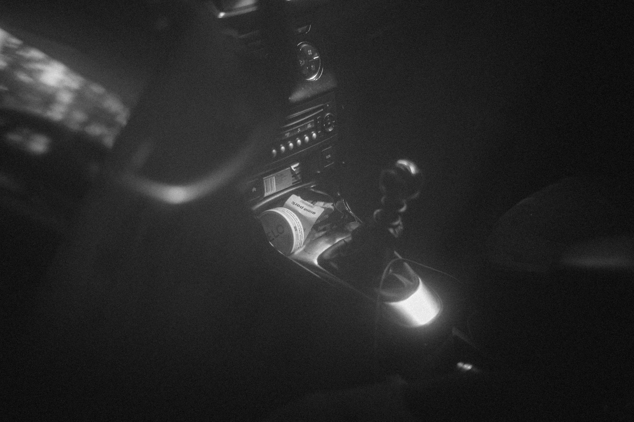 Black and white photograph of a car interior seen through a window, showing personal objects left inside.