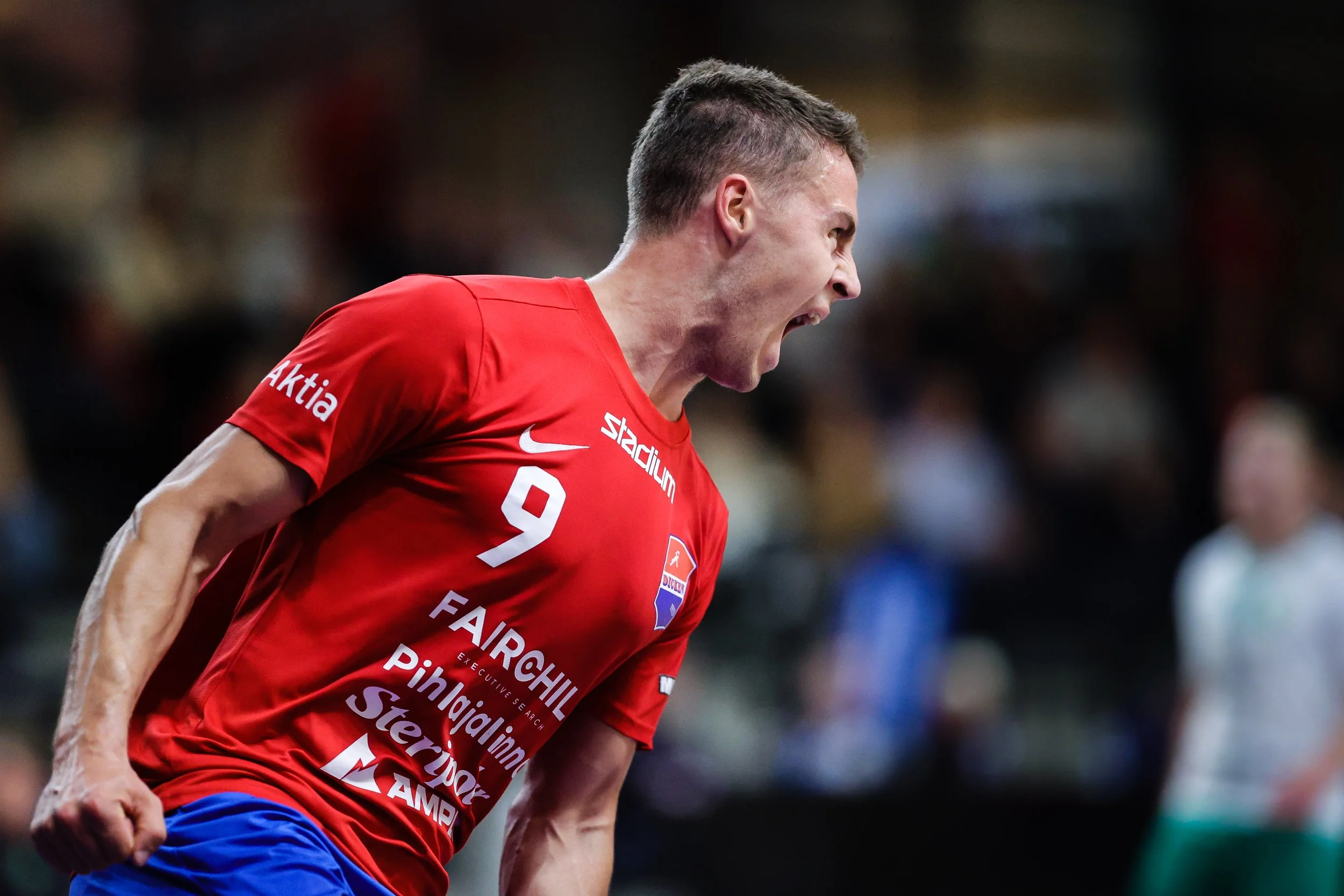 A male handball player in a red jersey with the number 9, yelling or celebrating during a match.