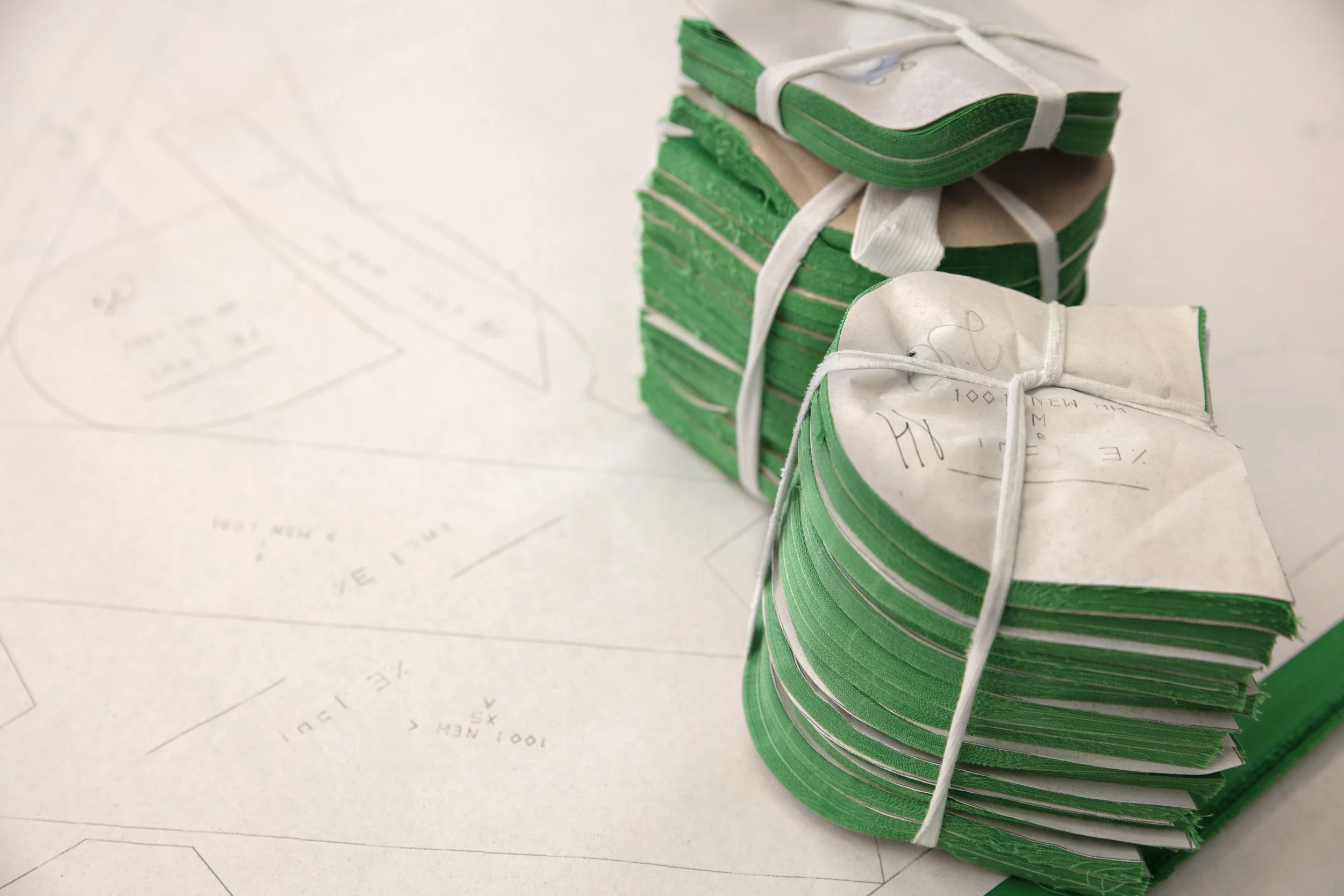 Stacks of green and white fabric pieces tied with white rubber bands on a white surface with sketches and notes.