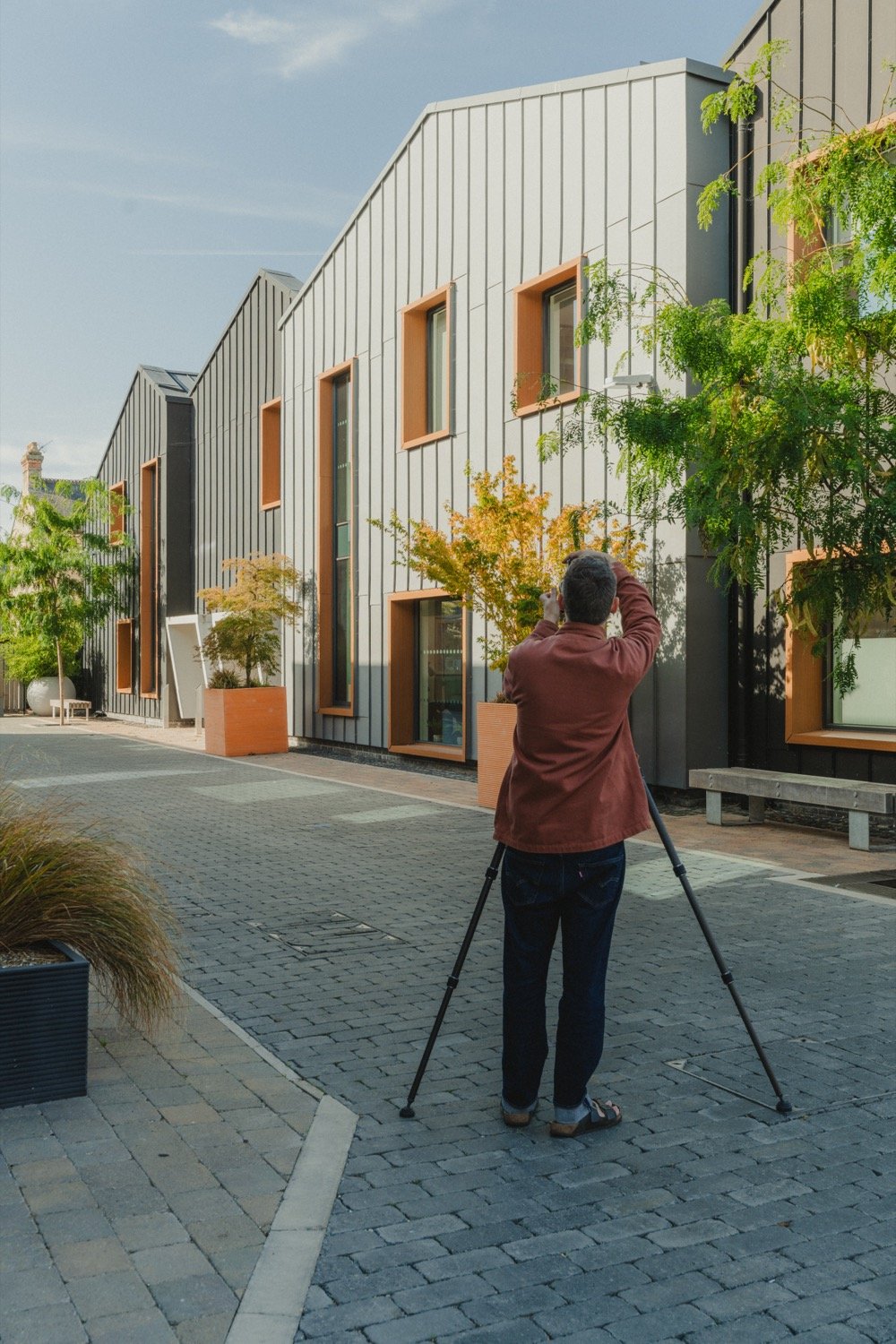 Matthew Smith photographing a row of new buildings along a cobbled lane at Old Swiss, Cambridge