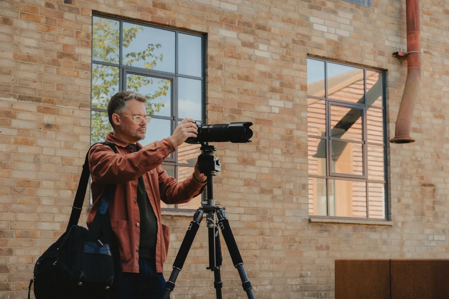 Matthew Smith shooting from a tripod beside a brick building with tall steel windows