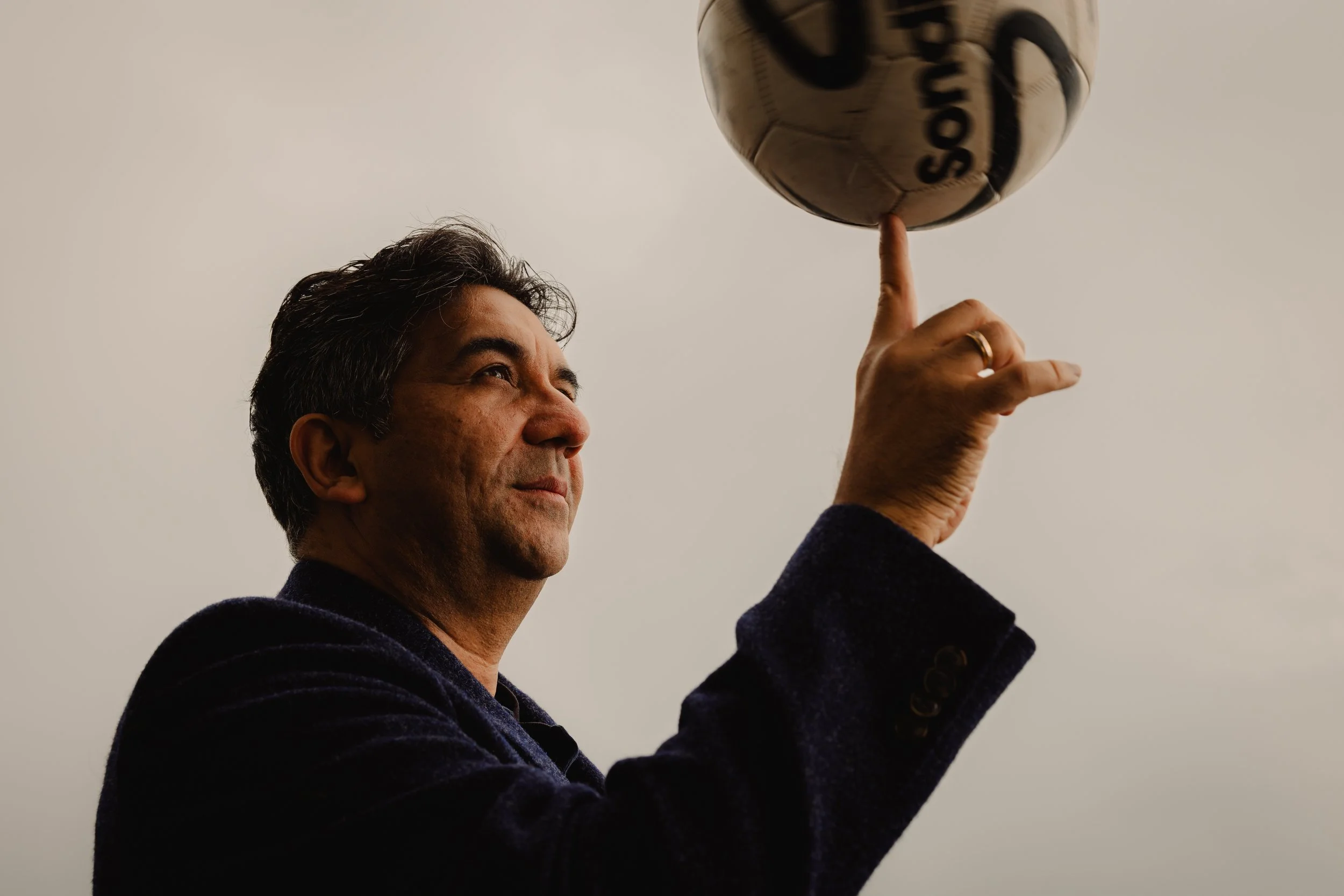 A man is spinning a soccer ball on his finger against an overcast sky.