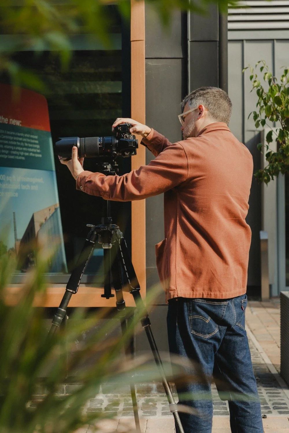 Matthew Smith adjusting his camera beside a site information board at Old Swiss, Cambridge