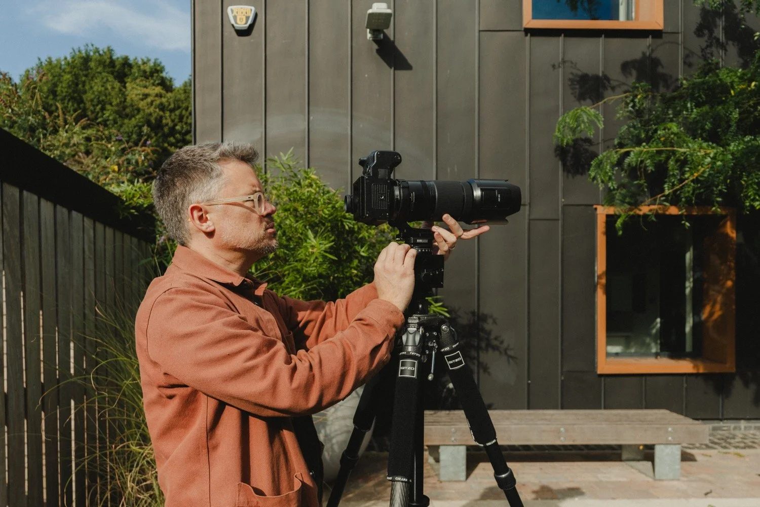Matthew Smith setting up a tripod beside dark metal cladding and planting