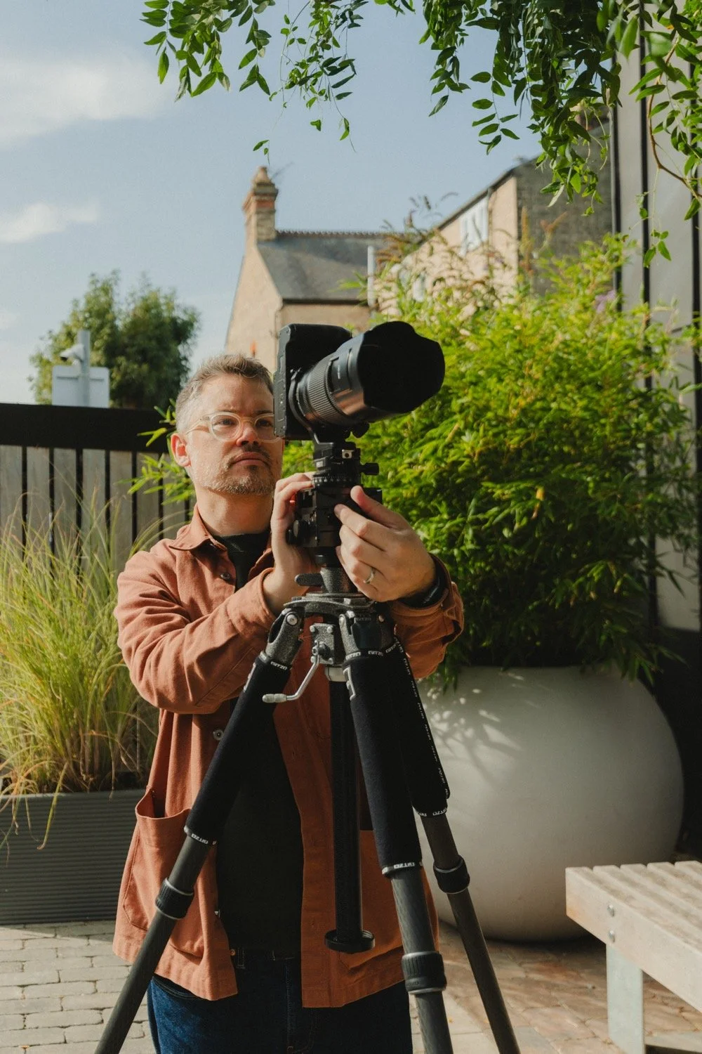 Matthew Smith looking through his camera on a tripod among large planters