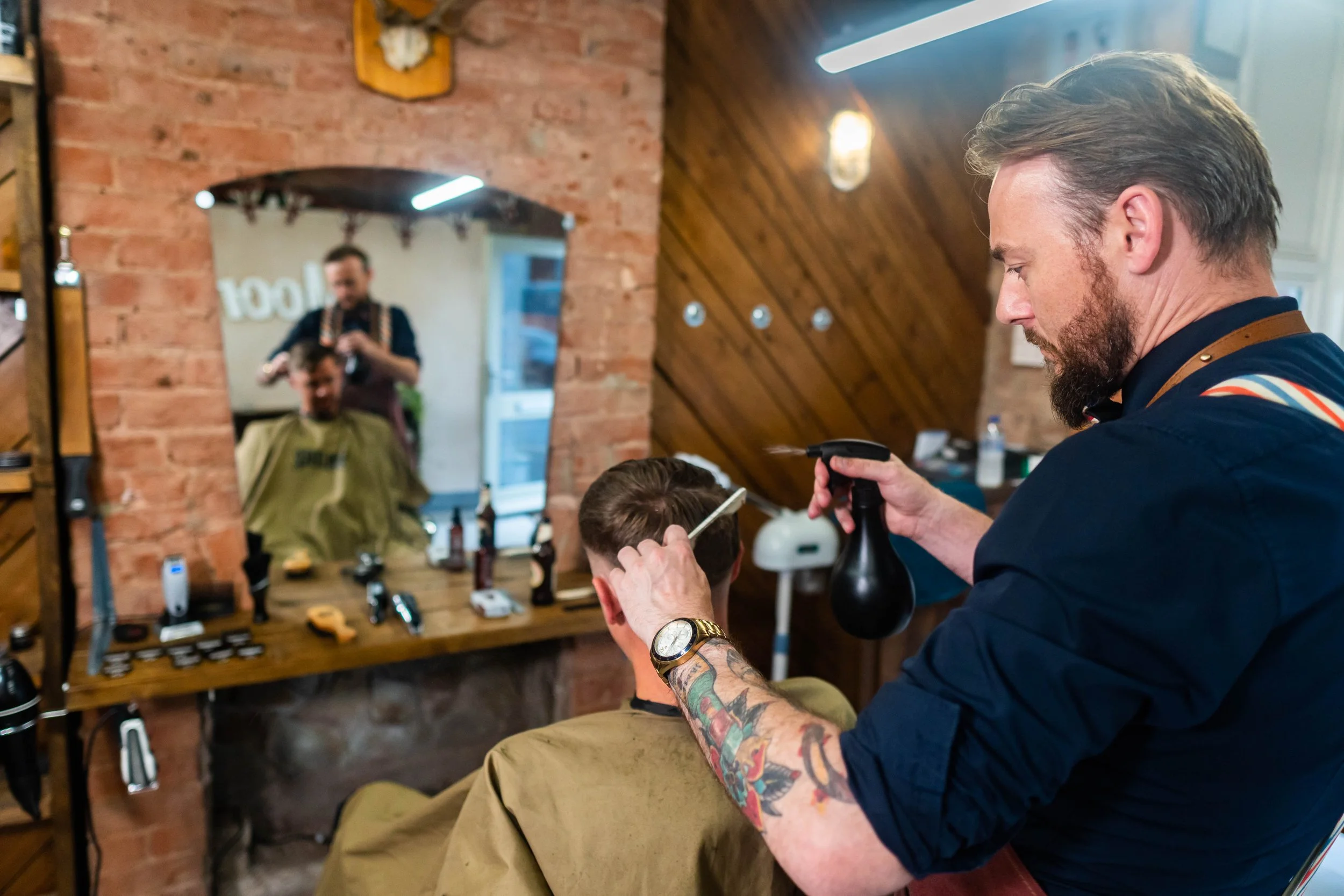 Barber cutting a man's hair in a cozy wooden and brick barbershop with a mirror reflecting the barber and customer.