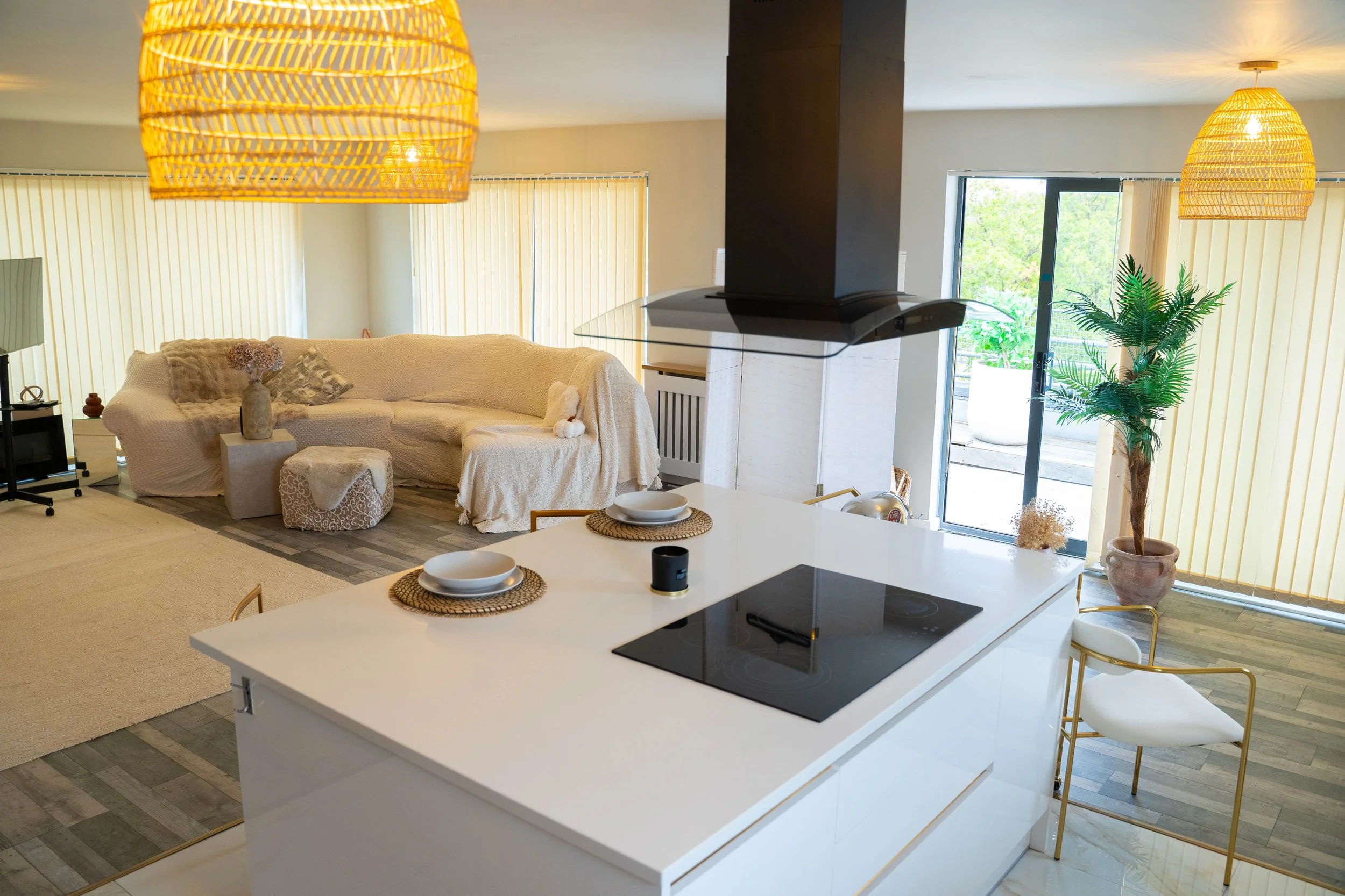 Open-concept living room and kitchen with beige sectional sofa, wooden accents, large sliding glass doors, potted plant, and pendant lights.