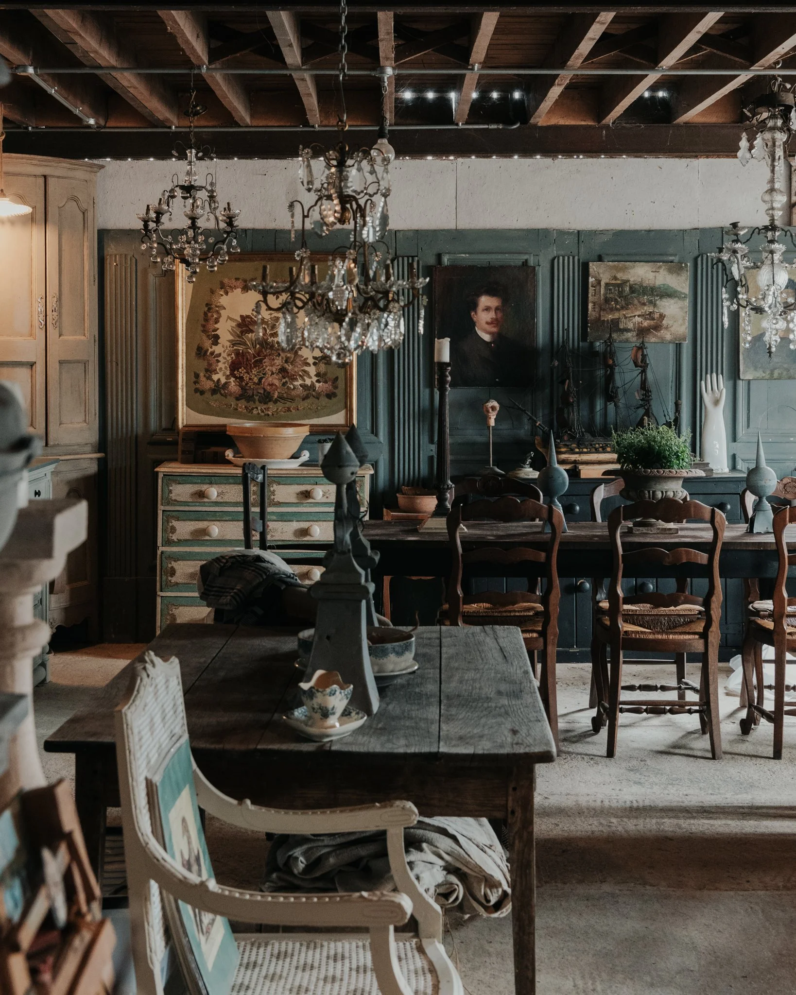 Interior of a vintage-style dining room with chandeliers, wooden tables, chairs, and decorative artwork and portraits on the walls.