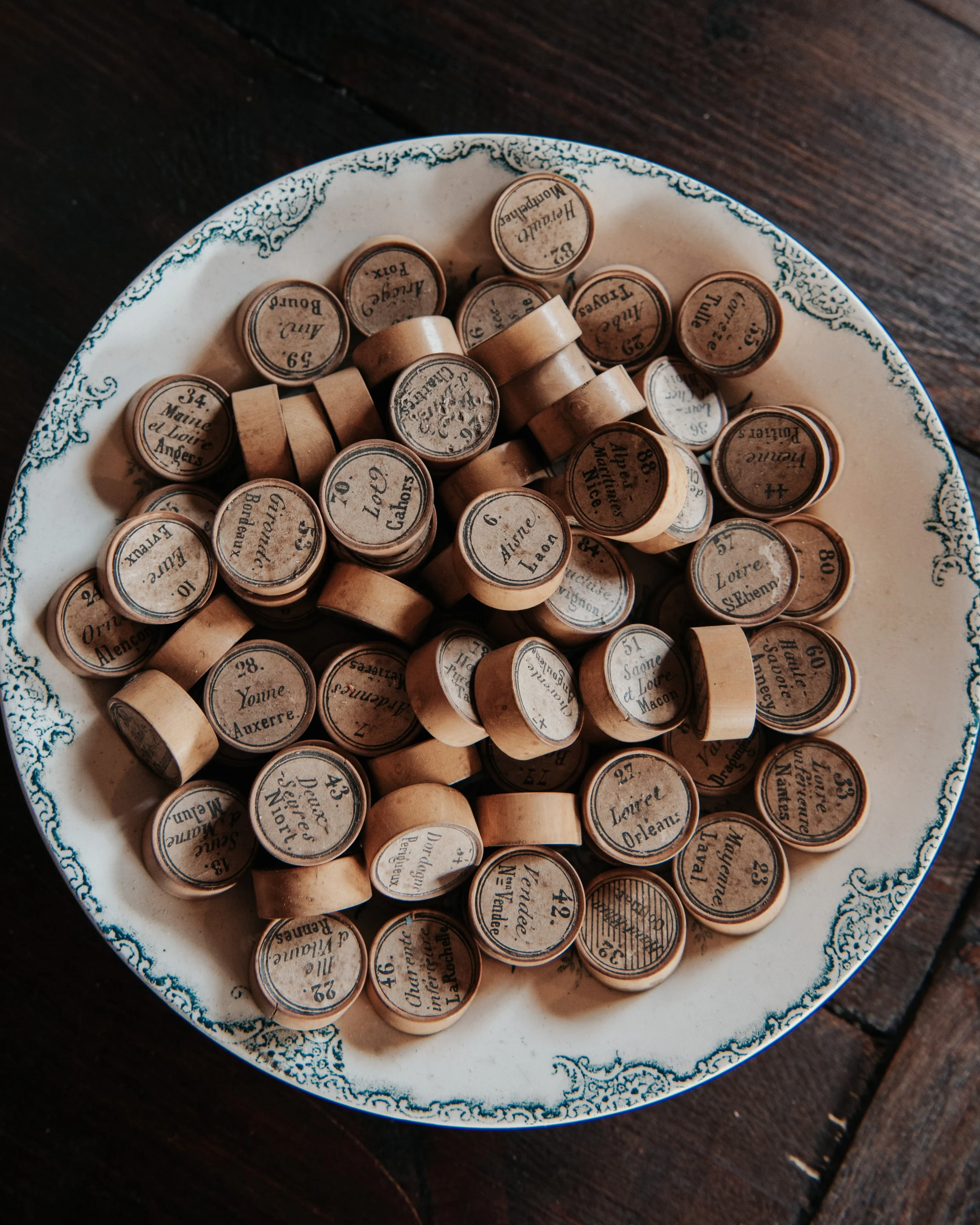 A decorative plate filled with vintage cabinetmaker wood stamps with black text, some labeled with French text, arranged on a dark wooden surface.