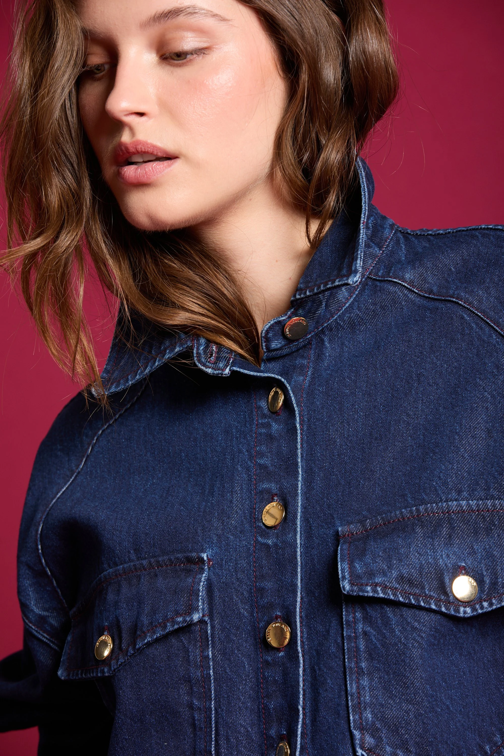 Ouverture partielle de la poitrine d'une femme portant une veste en denim bleu foncé, avec un fond rose.