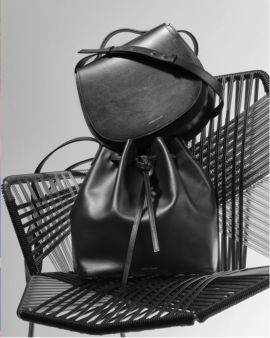 Deux sacs à main noirs en cuir placés sur une chaise design en métal noir, une chaise tressée.