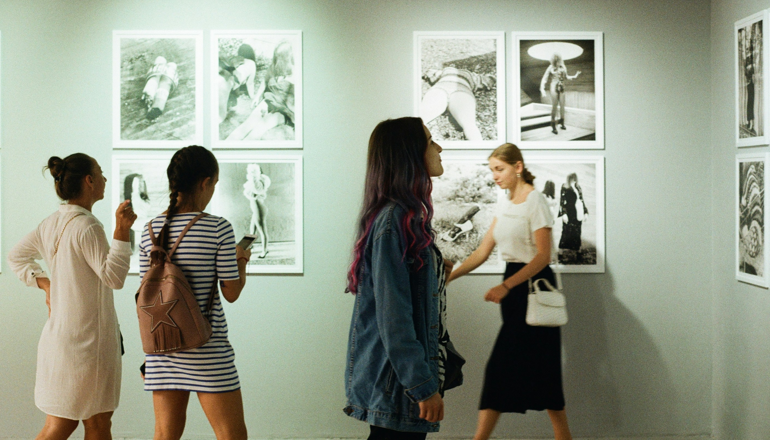Four women viewing black and white photographs in an art gallery with framed images on a light-colored wall.