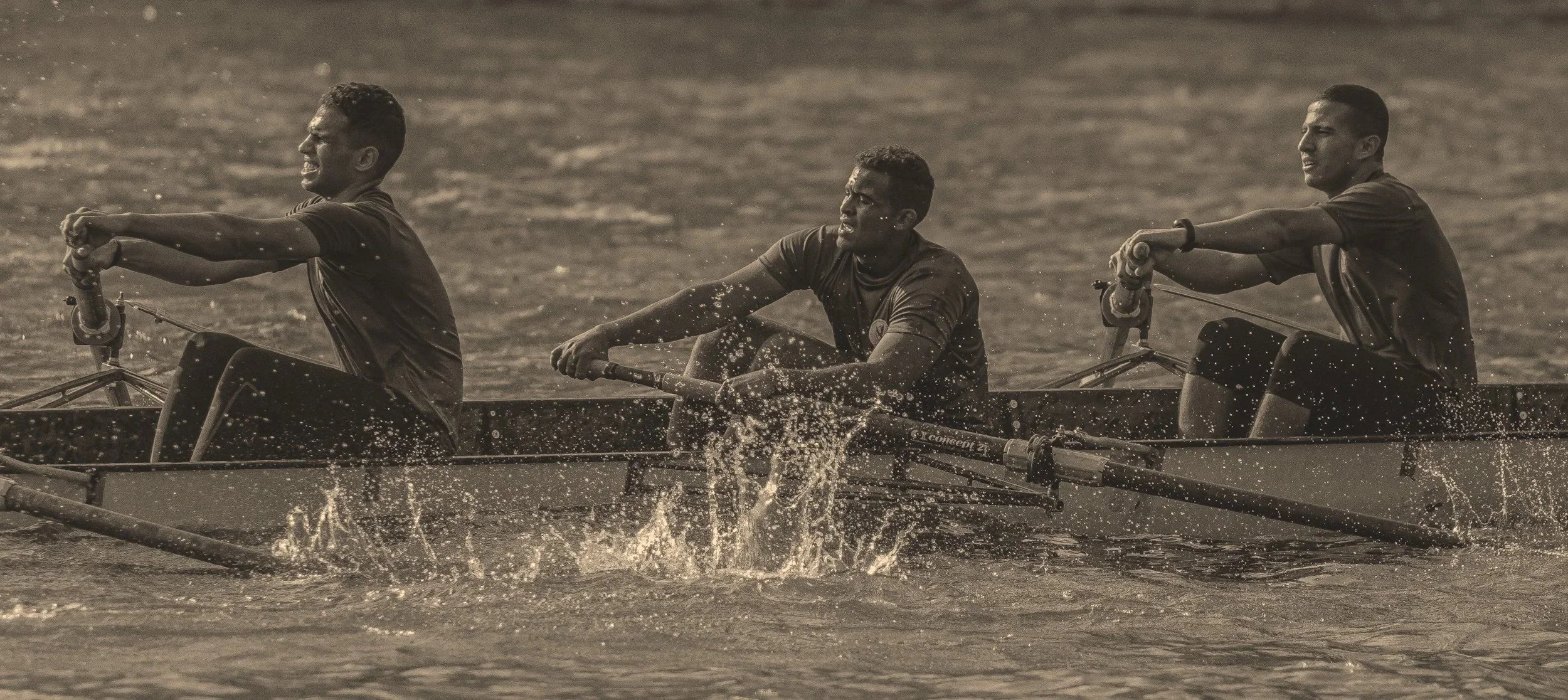 Rowers rowing a boat with effort while water splashes up from the oars