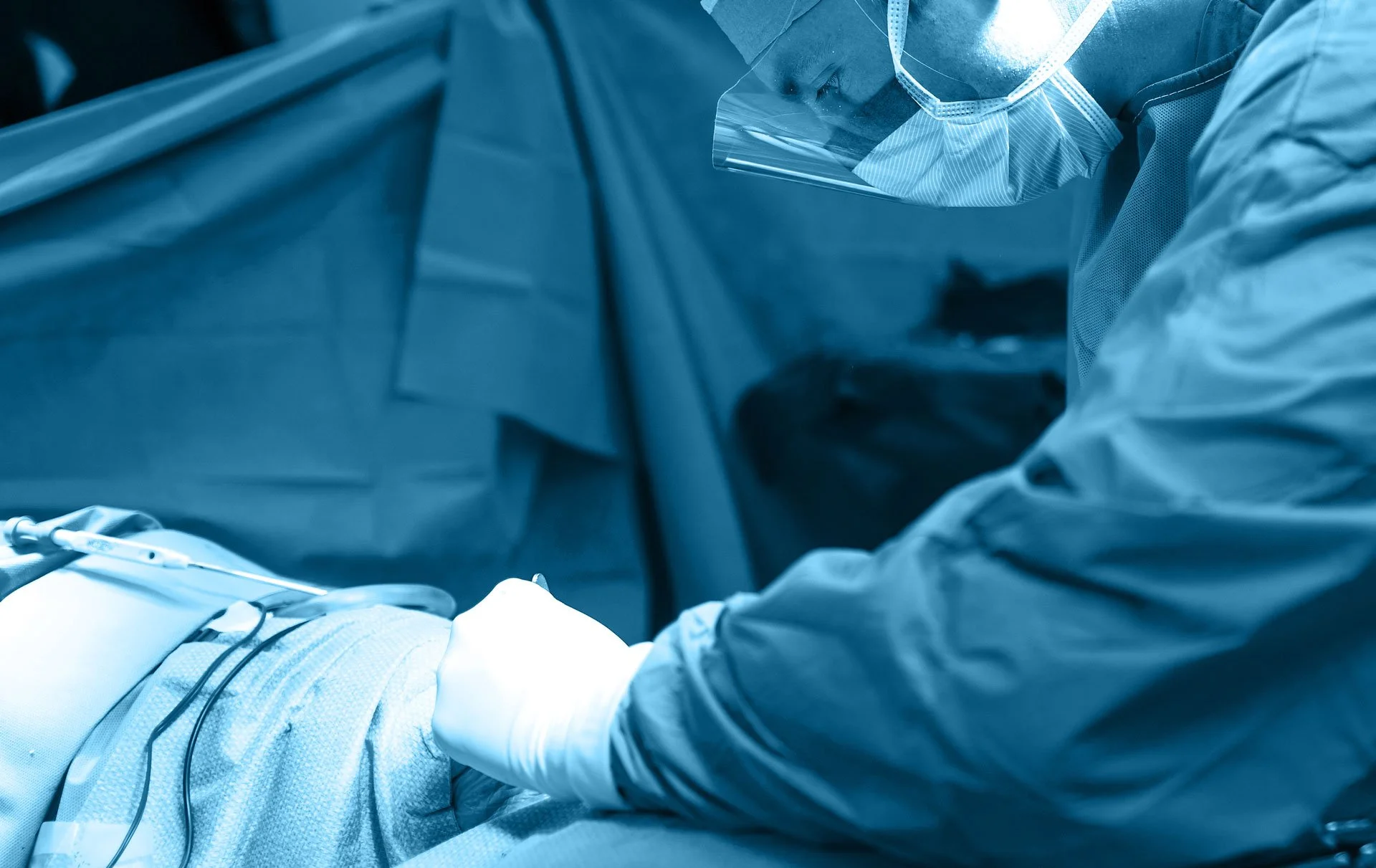 A medical professional performing surgery in an operating room, wearing protective gear including a mask and gloves.