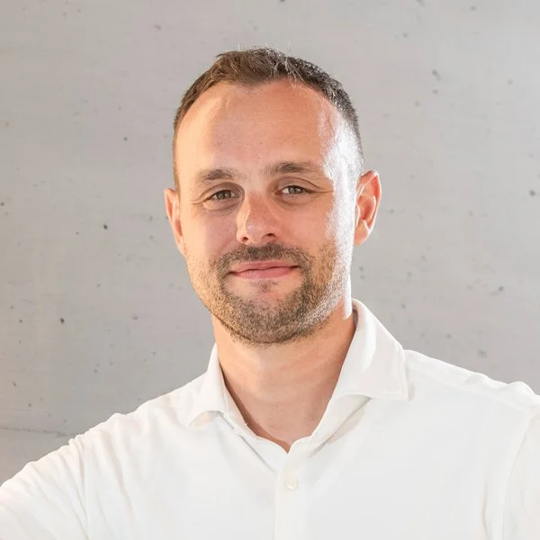 Porträt eines Mannes in Weiß vor einer grauen Wand im Fotostudio.