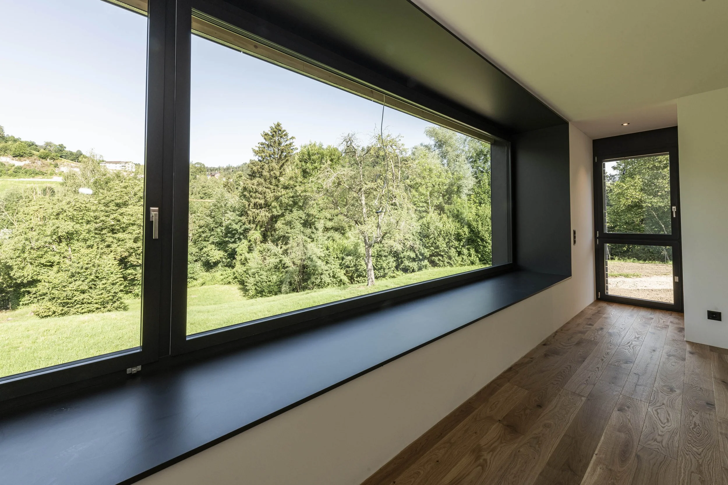 Innenraum mit großen Fenstern, Blick auf grüne Landschaft mit Bäumen, Holzboden