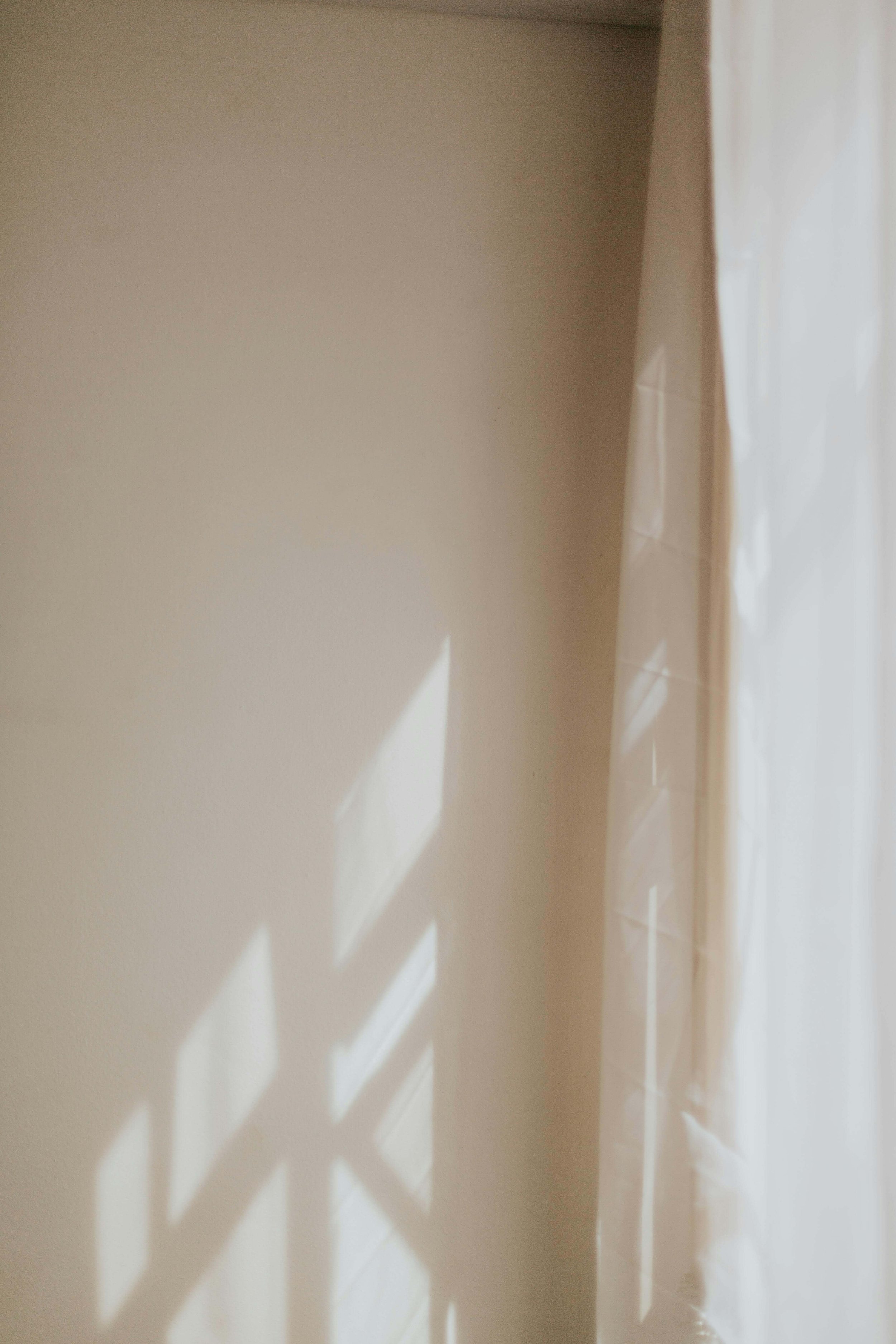 Sunlight casting geometric shadows on a plain wall next to a sheer curtain.