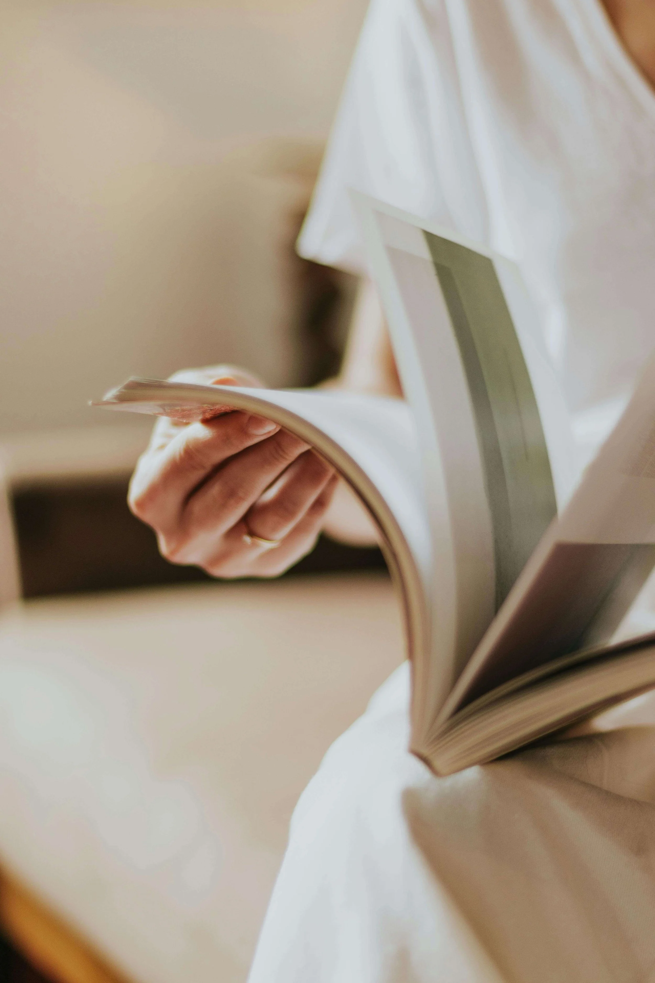 Person holding open magazine or book, wearing a white outfit, with a blurred background.