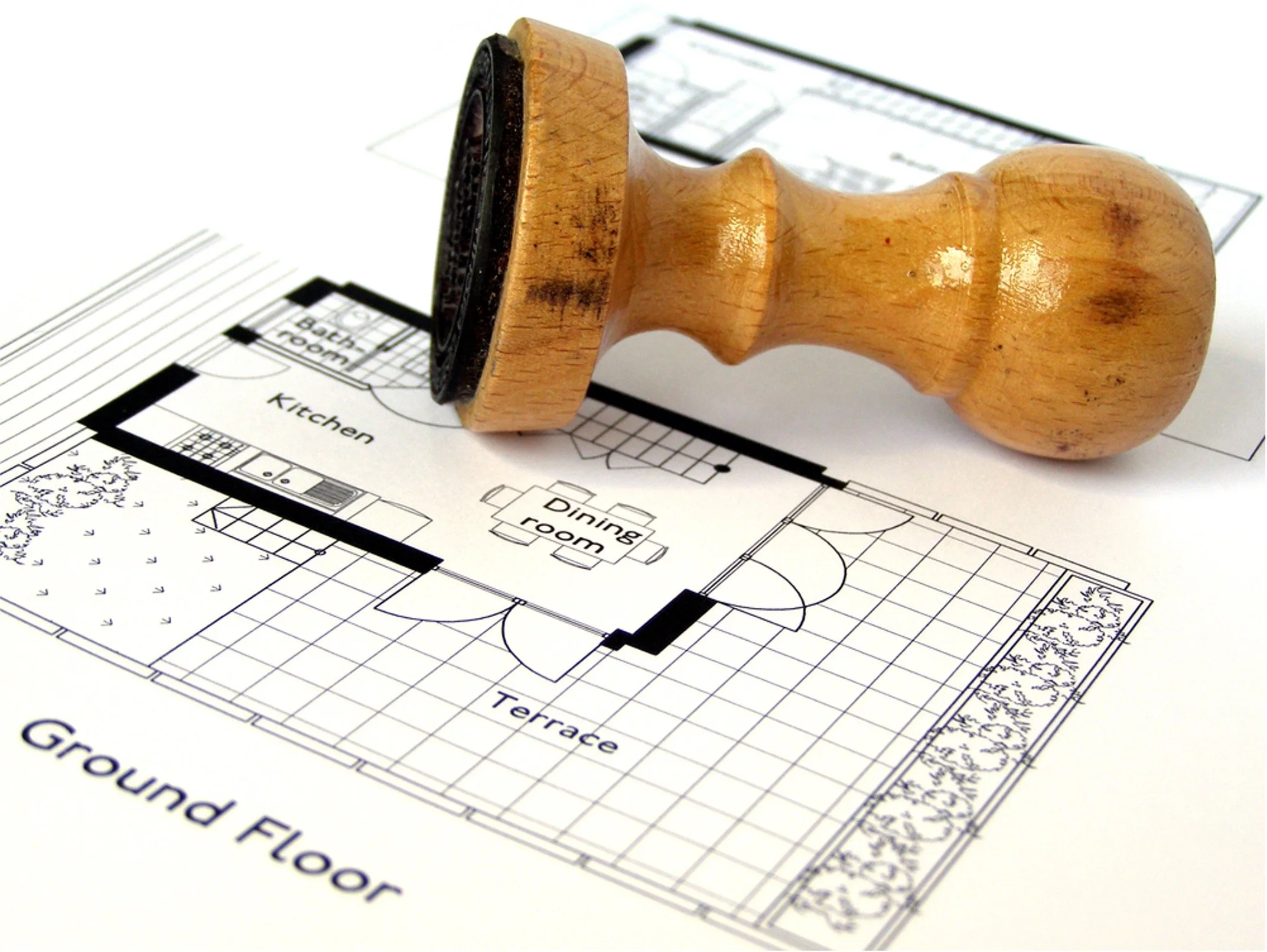 Exterior view of a modern house showing a black front door, an overhanging balcony with a metal railing, two windows, a brick column, and a textured white wall.