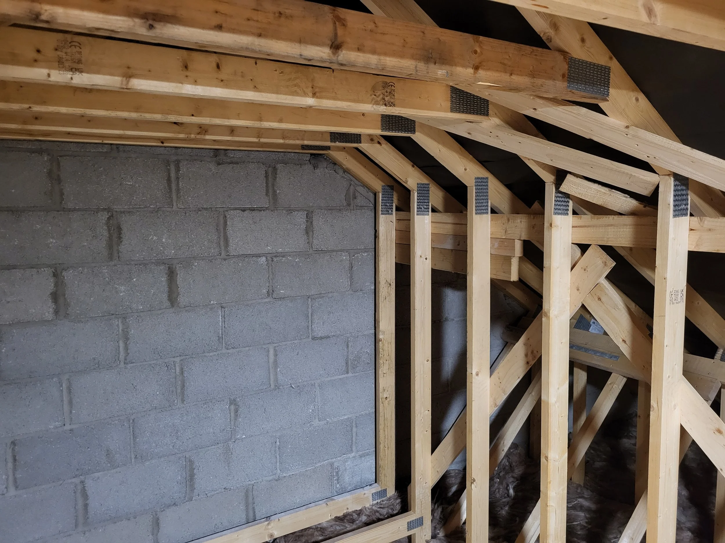 Interior construction of an attic showing unfinished wooden framing and a concrete block wall.