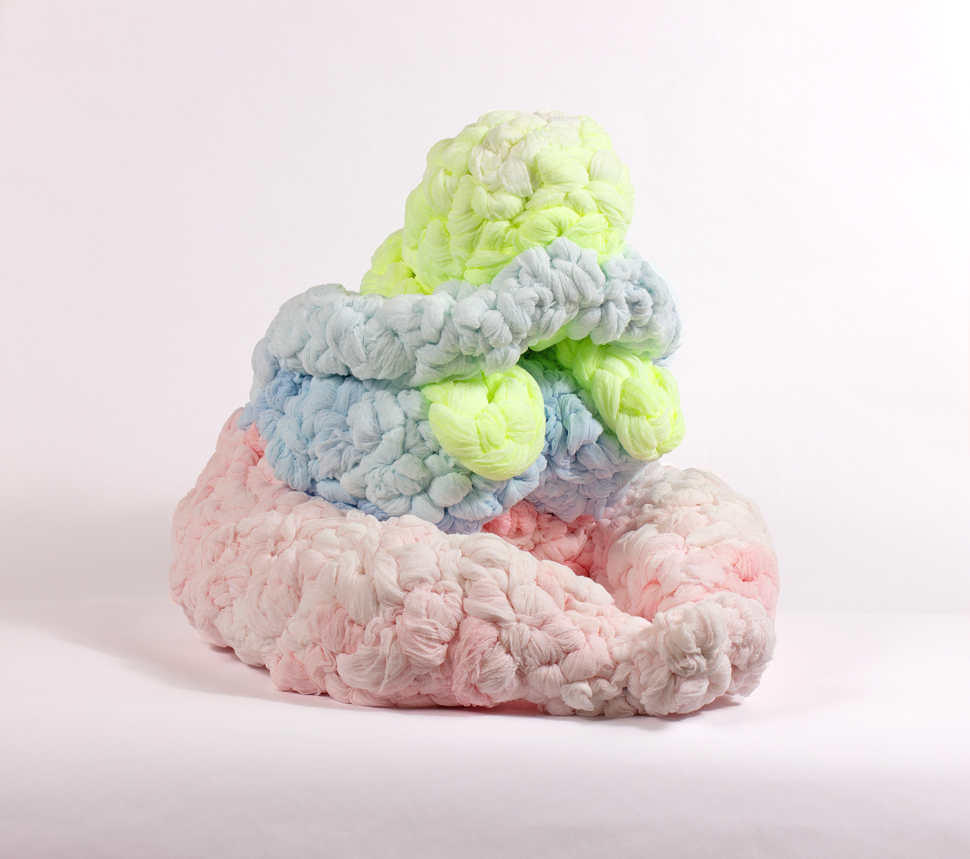 A colorful seated woman leaning over her crossed legs, textured cheesecloth stacked with the yellow at the bottom, pink in the middle, and blue on top.