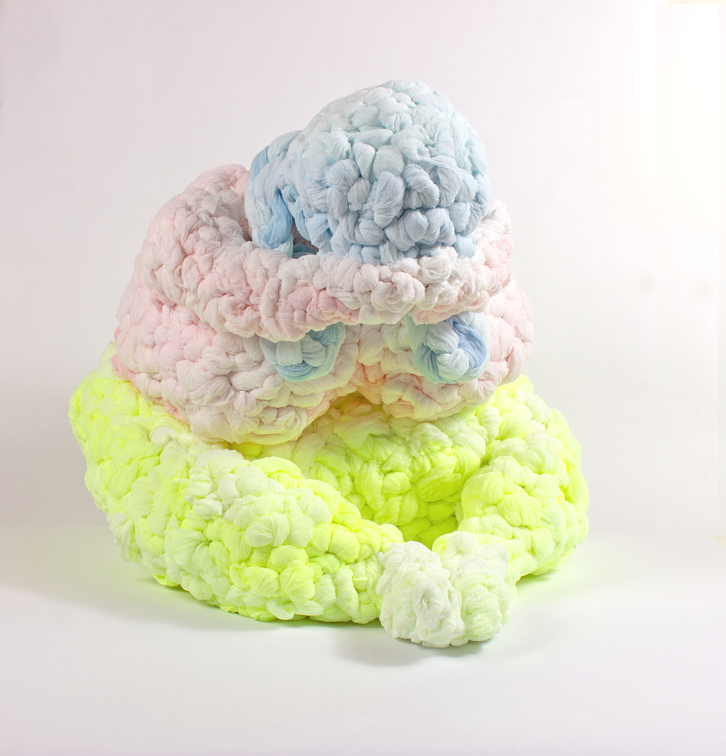 A colorful seated woman leaning over her crossed legs, textured cheesecloth stacked with the yellow at the bottom, pink in the middle, and blue on top.