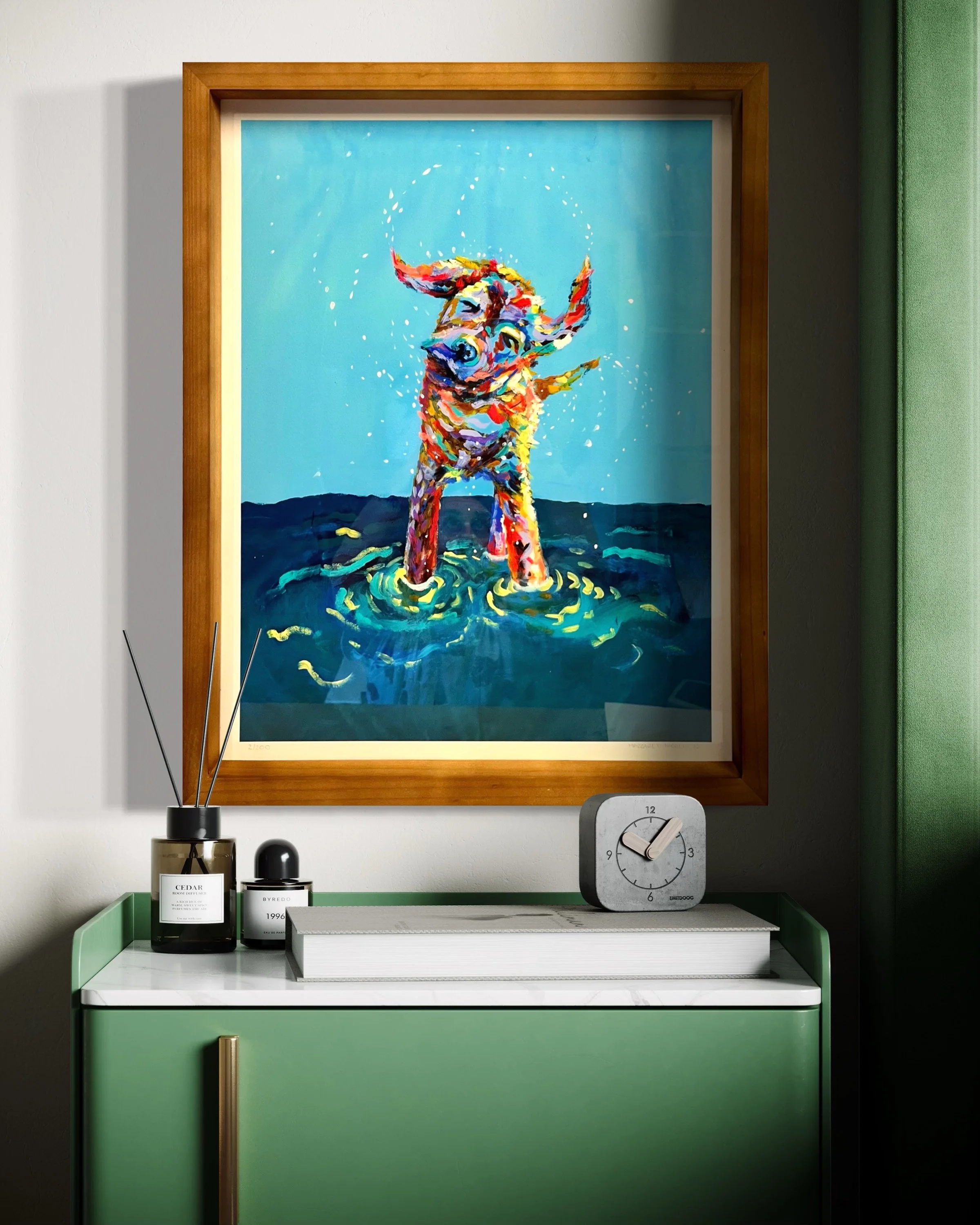 Framed colorful painting of a dog standing in water with waves and splashes, hung above a green cabinet with a clock, books, and candles.