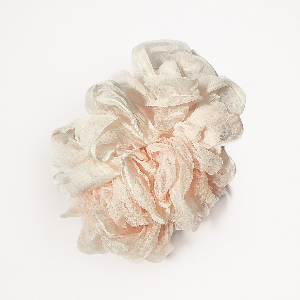A light-colored scrunchie made of soft, sheer fabric placed on a plain white background.