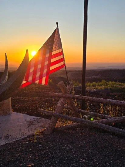 American flag hanging on a wooden fence at sunset.